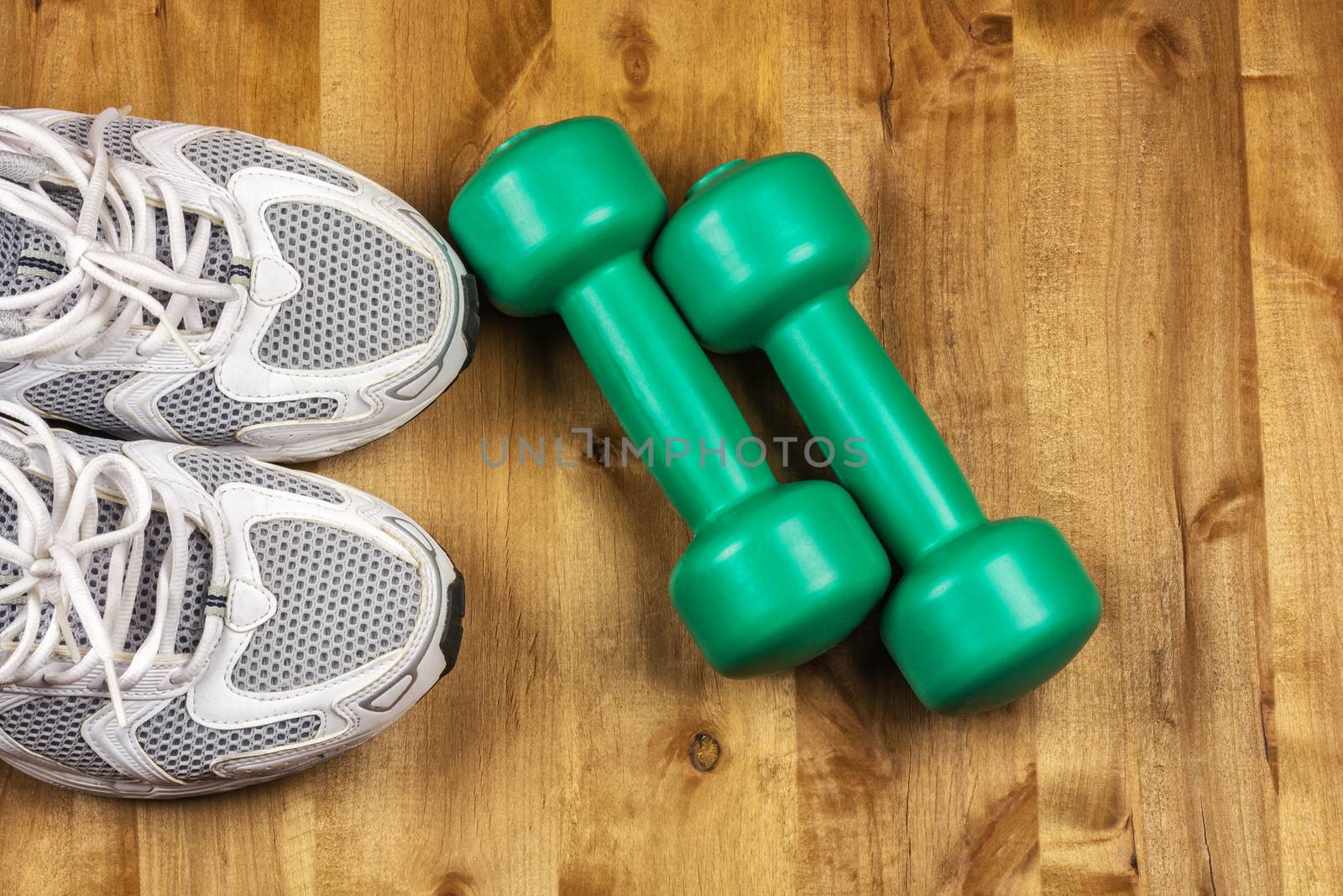 On the wooden floor are two dumbbells and a pair of white sneakers