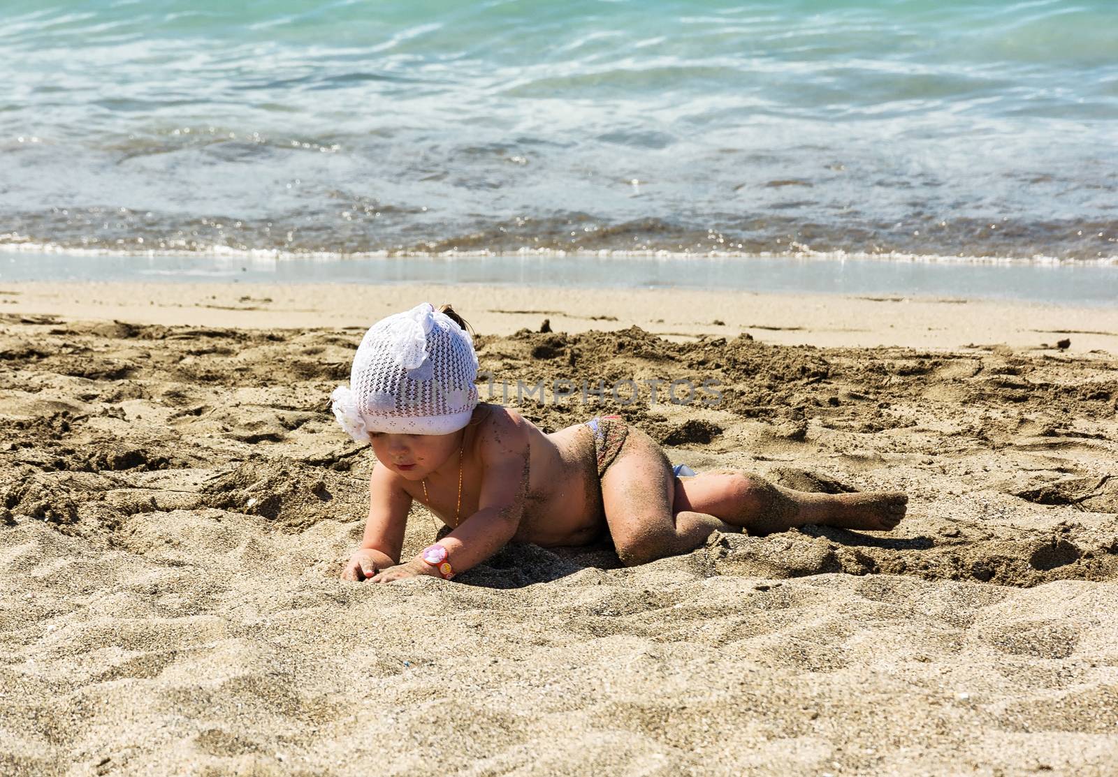 The girl of 3 years lays on sand of a beach near water by Grommik