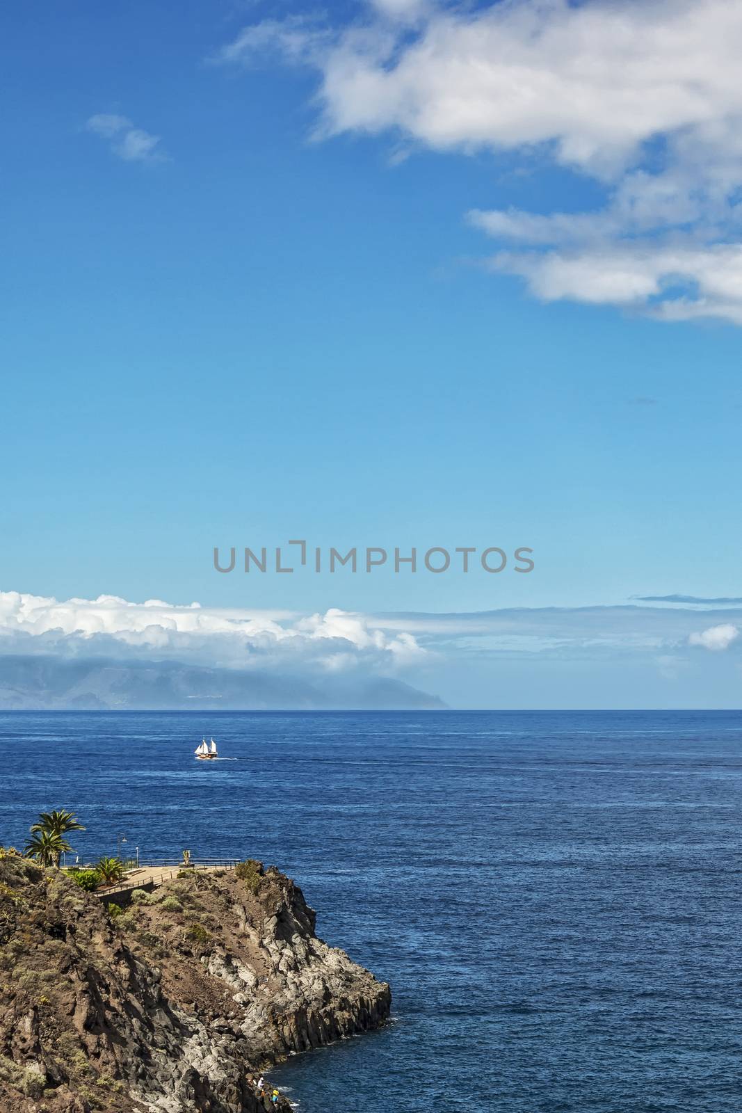 Along the rocky shore a sailboat sails with white sails