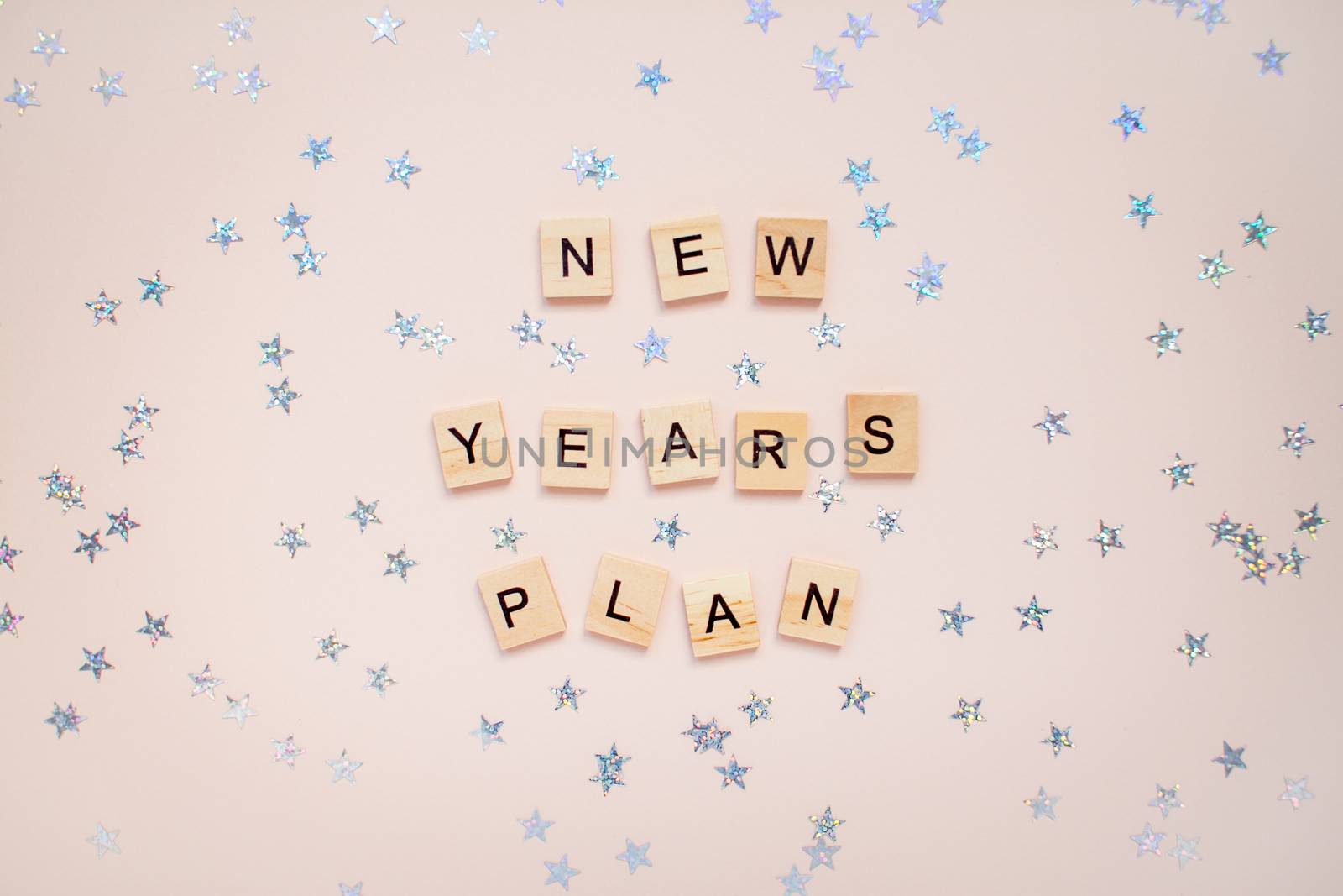 The inscription new years plan from wooden blocks on a light pink background. Silvery stars on a light pink background.