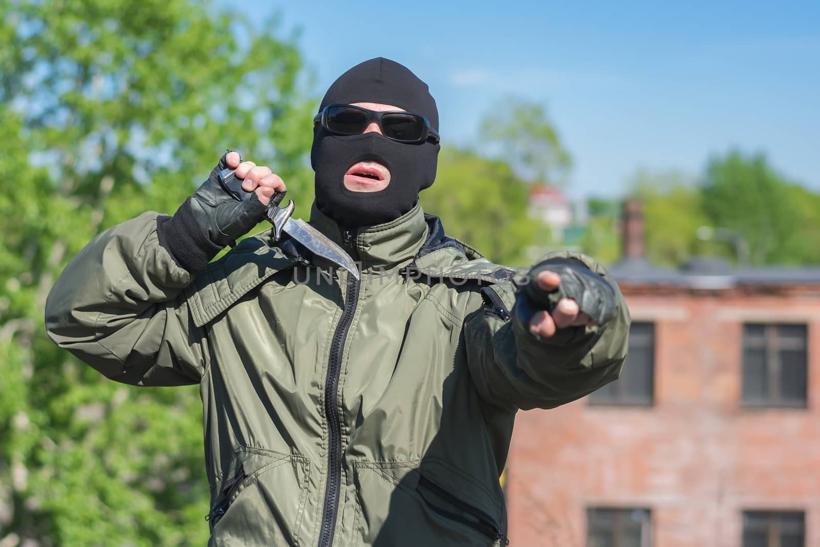 Masked bandit shows threatening gestures with a knife