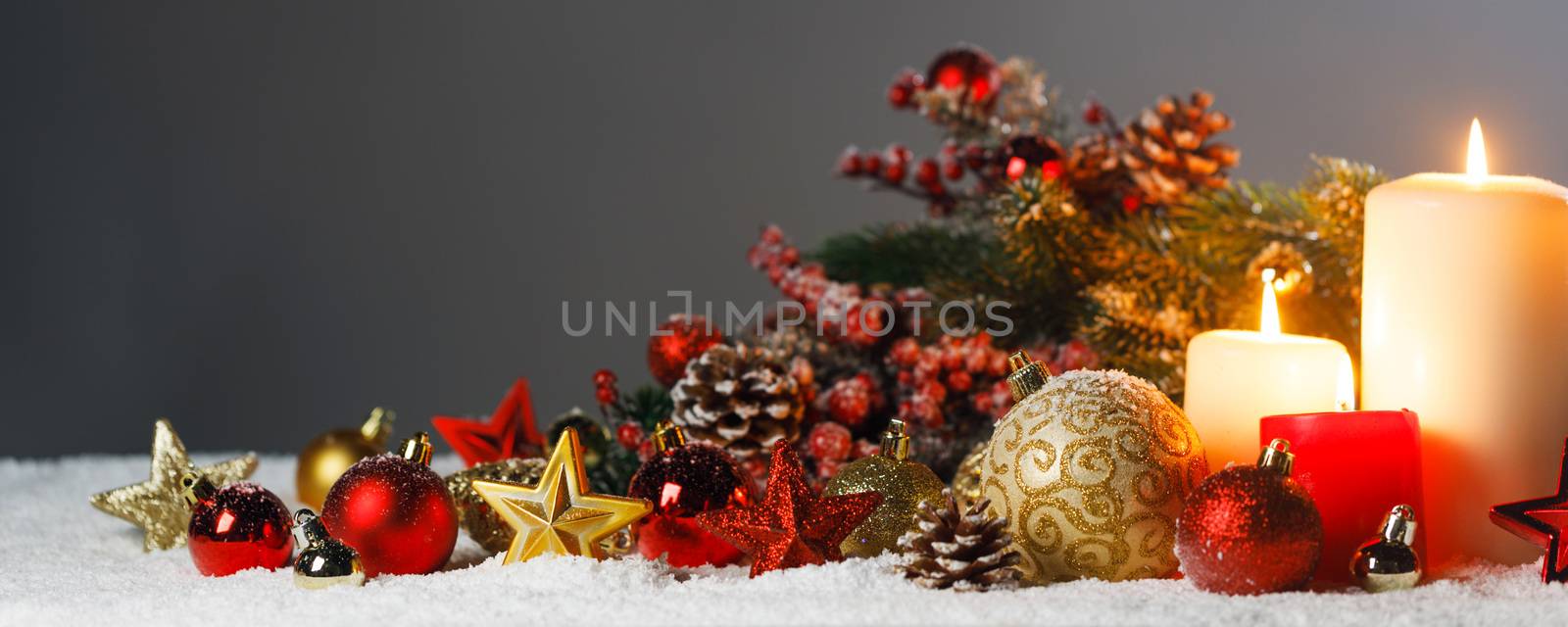 Christmas candles with traditional decorative stars , red baubles , pine cones and green branches on snow