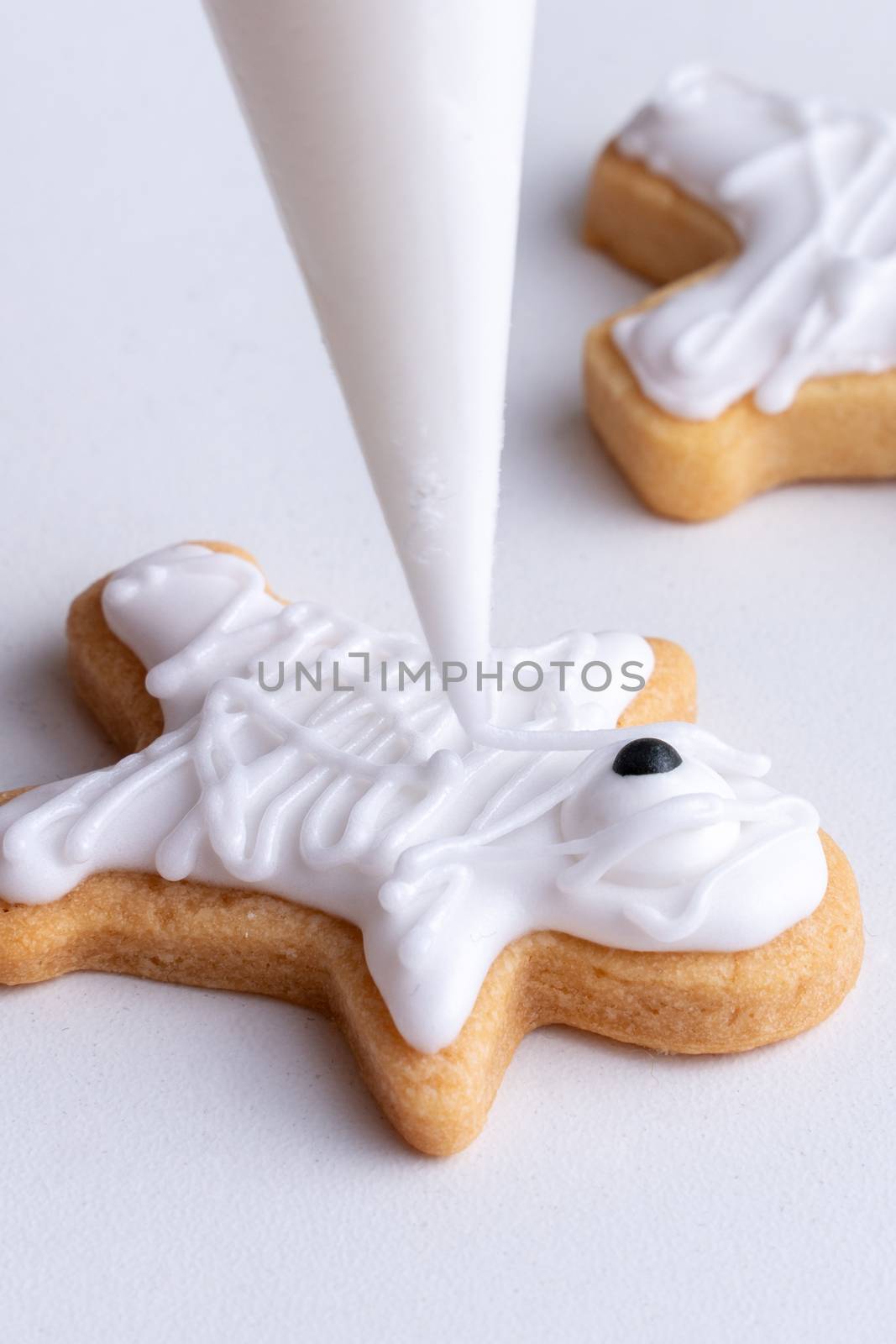 Close up of decorating cute Halloween gingerbread cookies with frosting icing cream topping bag.