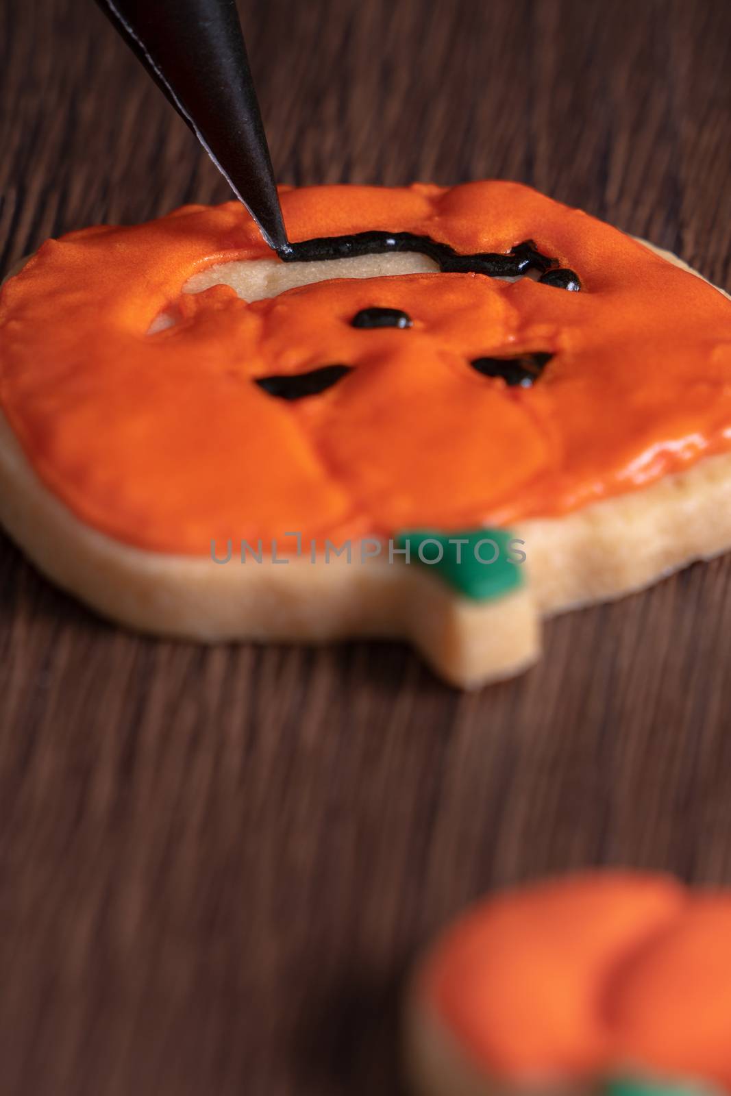 Close up of decorating cute Halloween pumpkin gingerbread cookies with frosting icing cream topping bag.