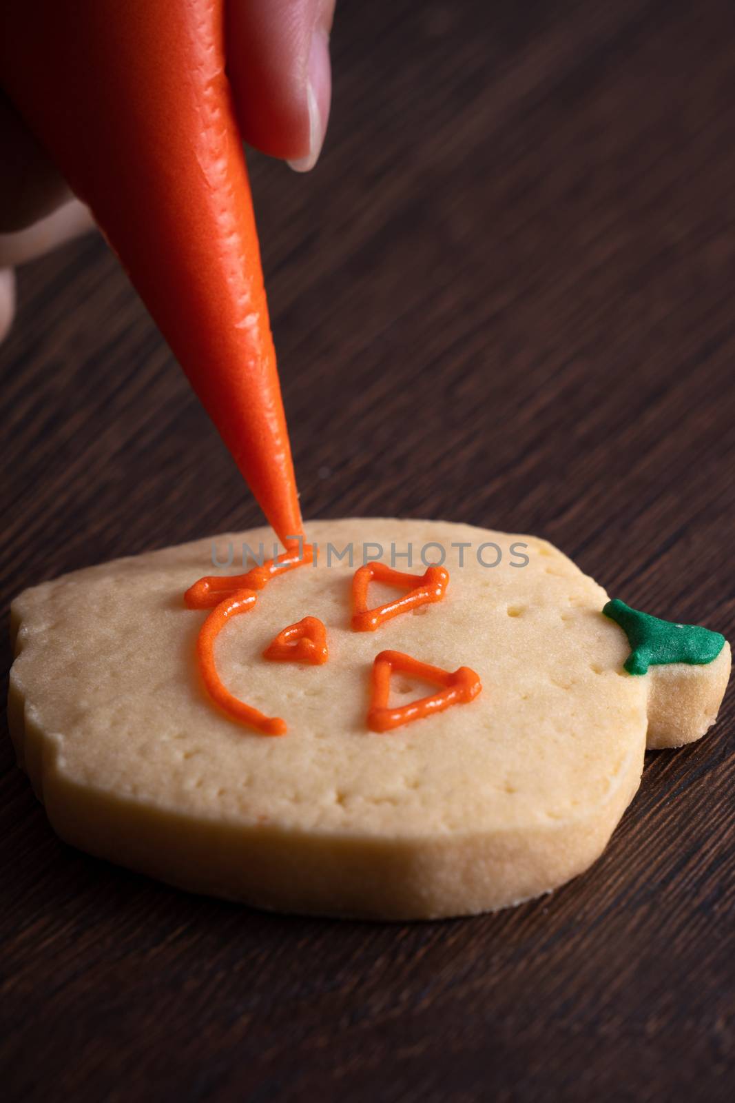 Close up of decorating cute Halloween pumpkin gingerbread cookies with frosting icing cream topping bag.