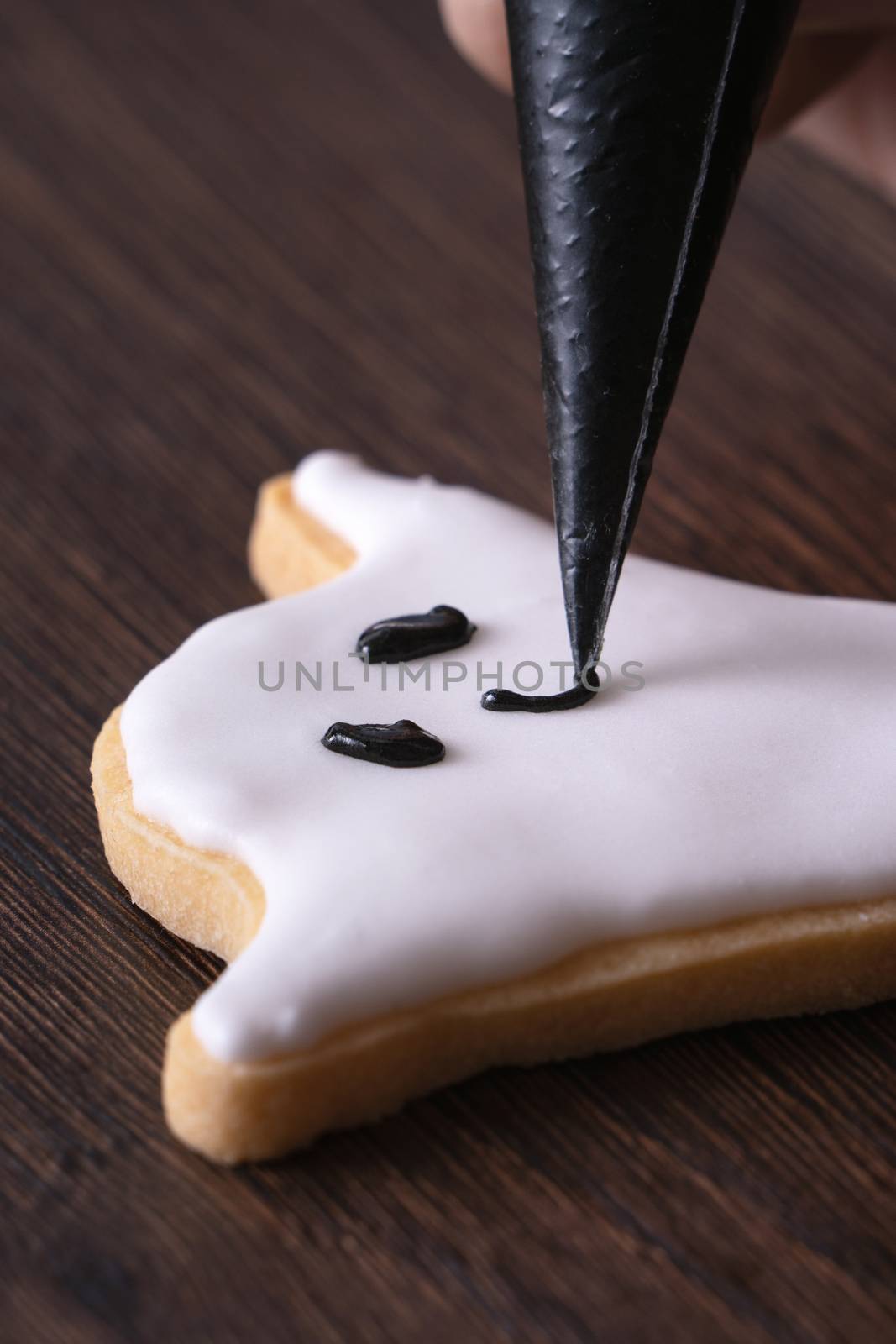 Close up of decorating cute Halloween ghost gingerbread cookies with frosting icing cream topping bag.