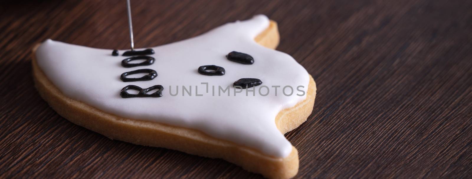 Close up of decorating cute Halloween ghost gingerbread cookies with frosting icing cream topping bag.