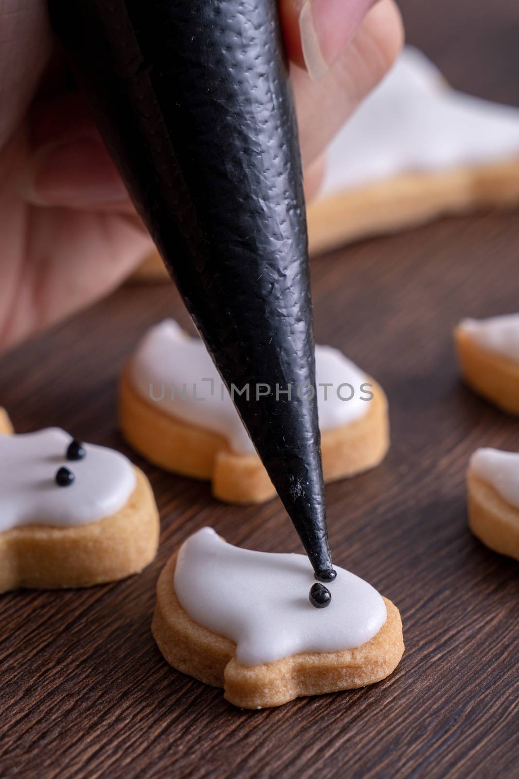 Close up of decorating cute Halloween ghost gingerbread cookies with frosting icing cream topping bag.