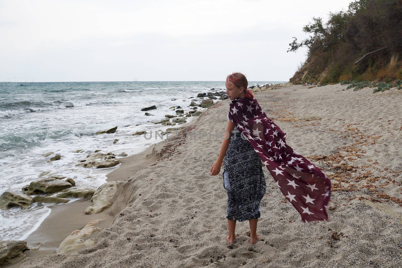 teenage girl with a big scarf walks around the empty beach by Annado