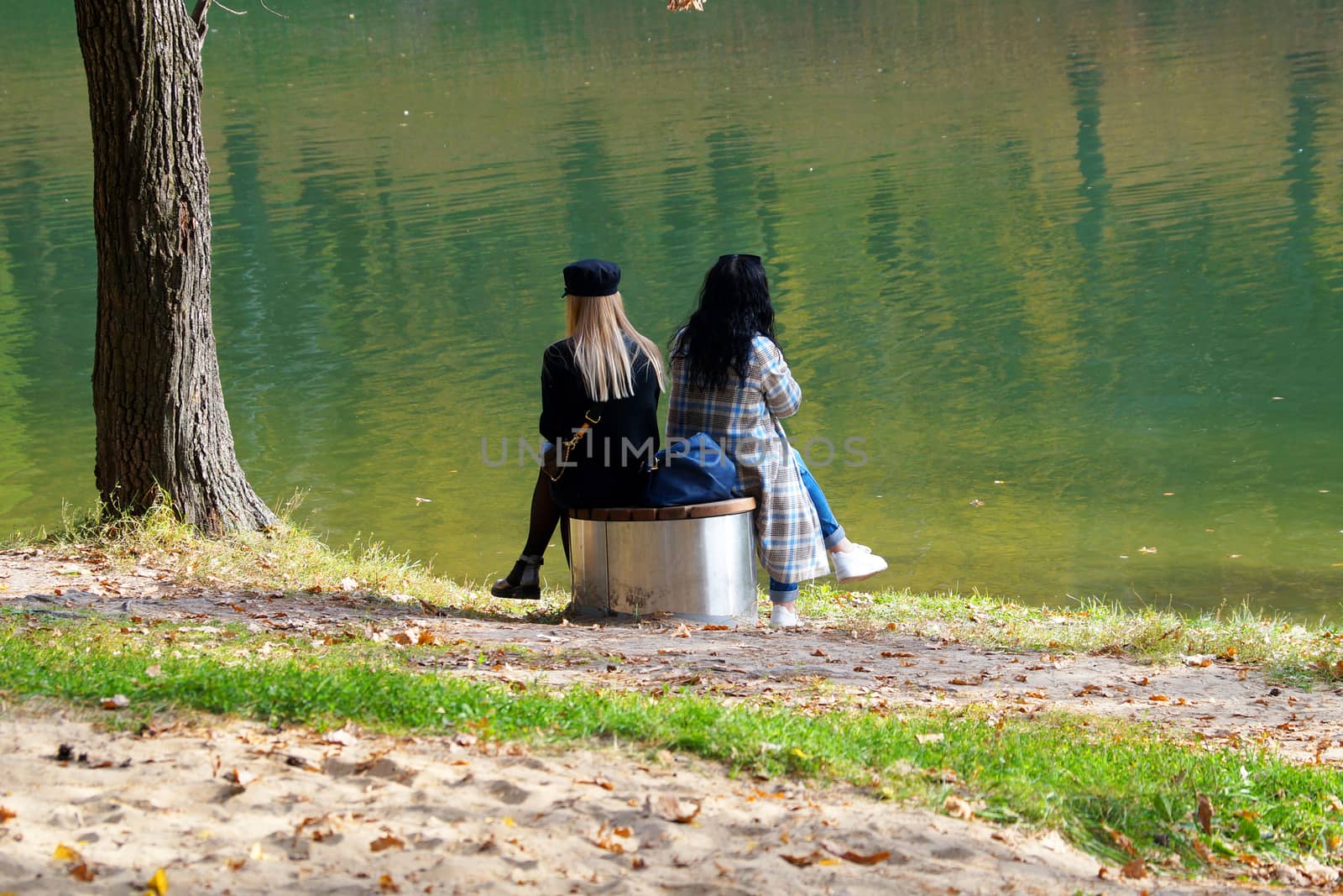 two girls are sitting next to each other on a bench by the lake in an autumn park, LGBT by Annado