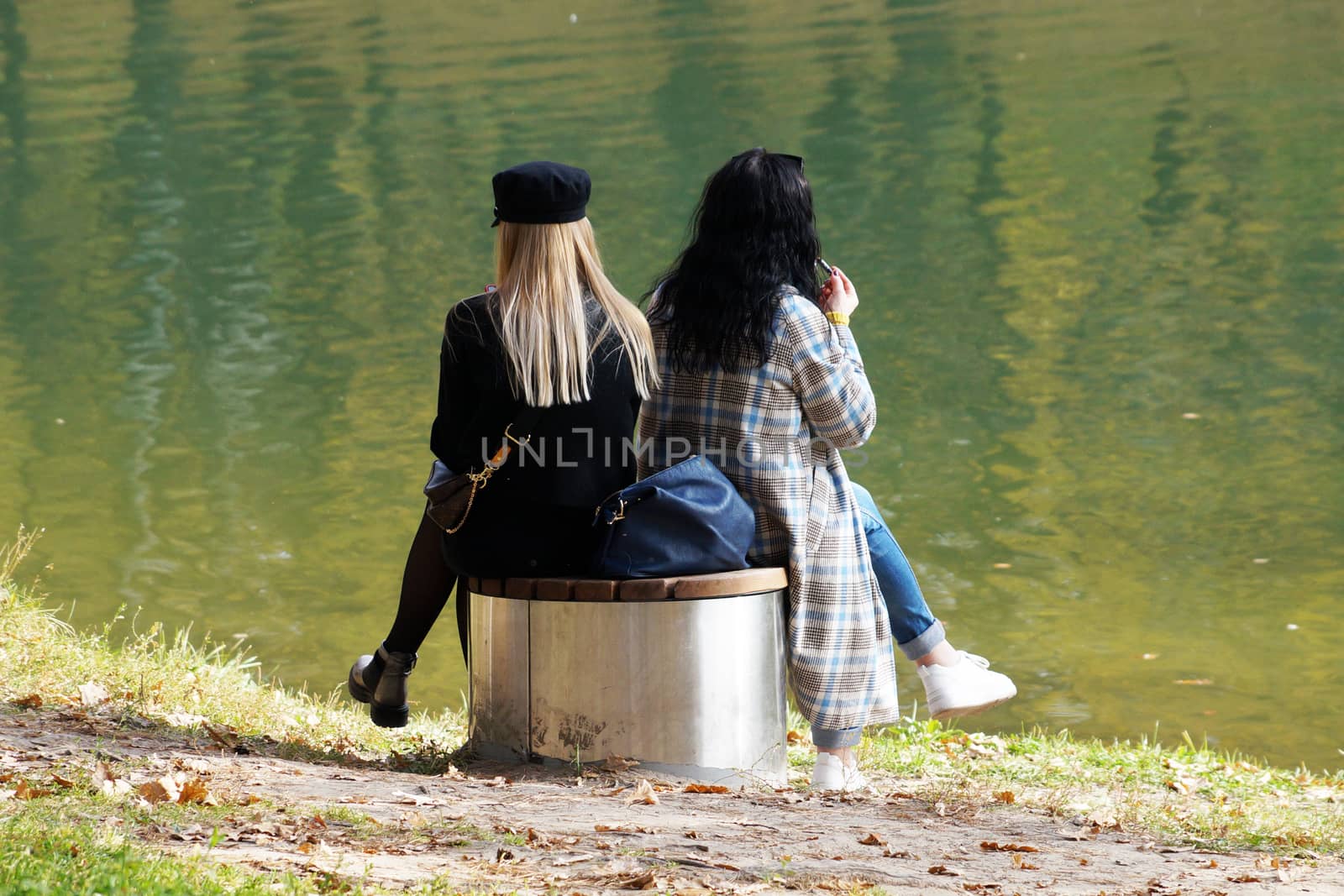 two girls are sitting next to each other on a bench by the lake in an autumn park, LGBT by Annado