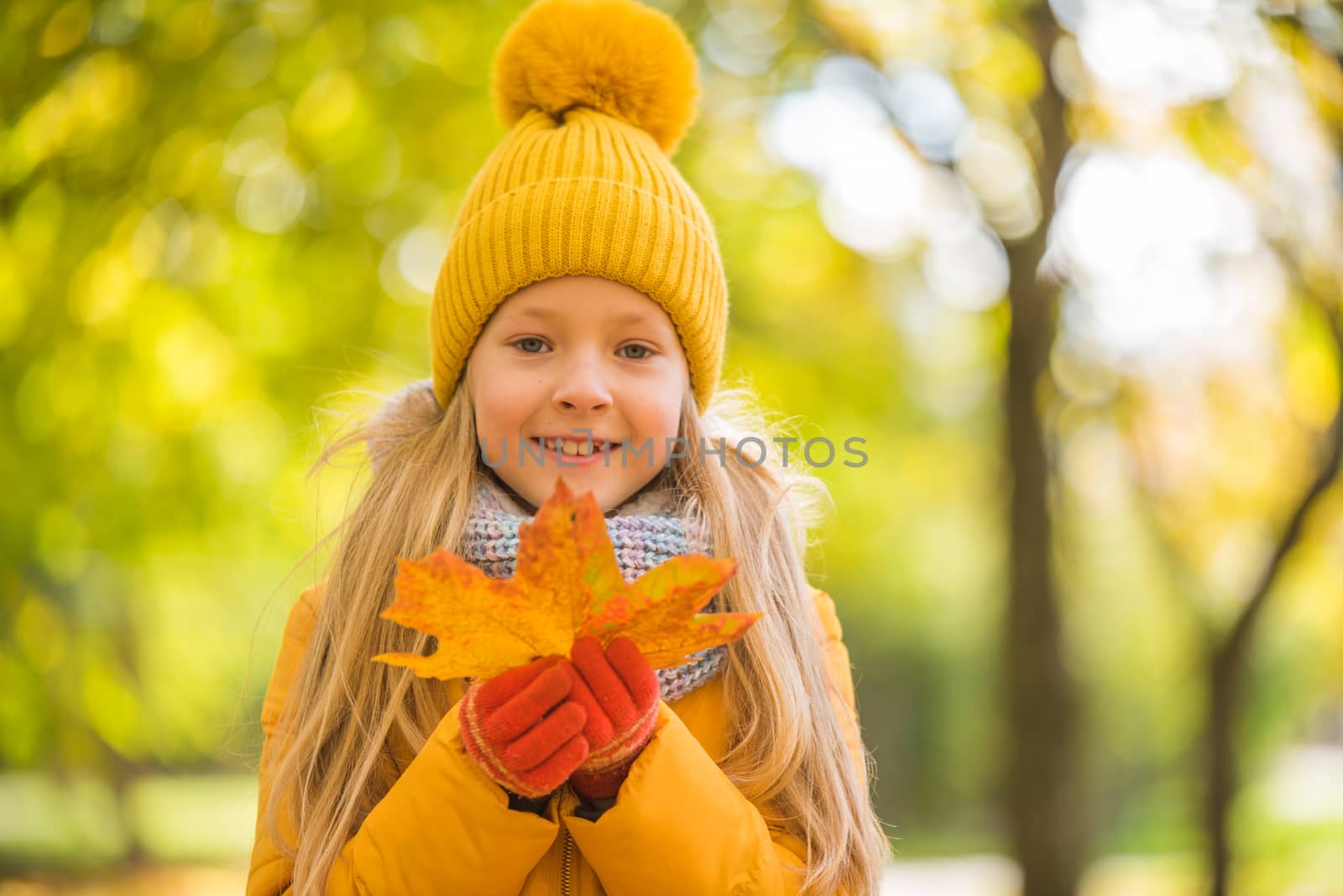 Little girl with blond hair in autumn background in yellow clothing