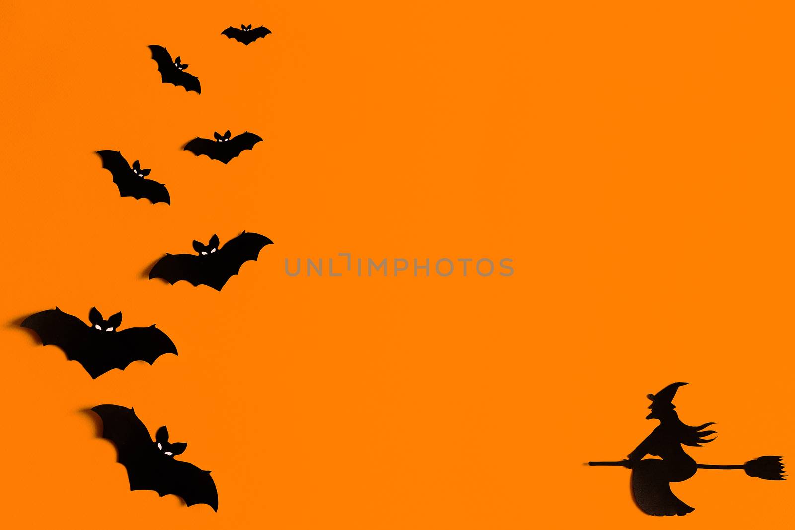 Silhouettes of a flock of bats and a witch flying on a broom made of black paper on an orange background. Halloween greeting template with copy space. Flat lay for your design. ready-made template by Pirlik
