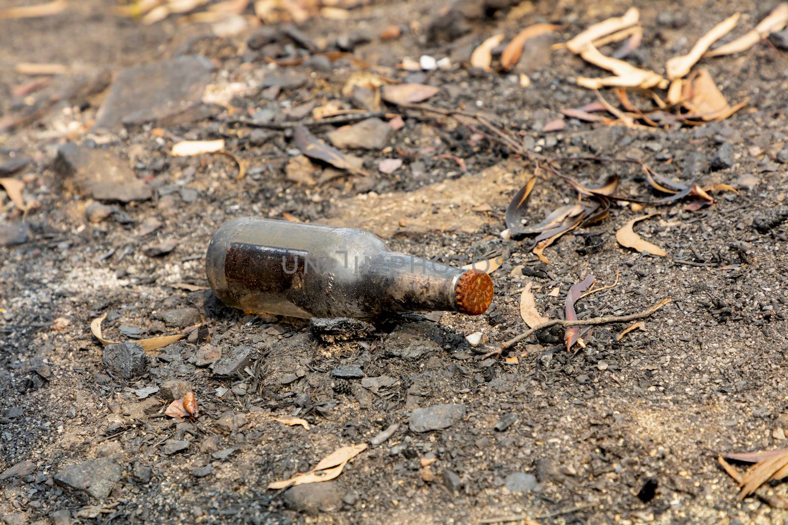 A glass drinking bottle on the ground after bushfires in regional Australia