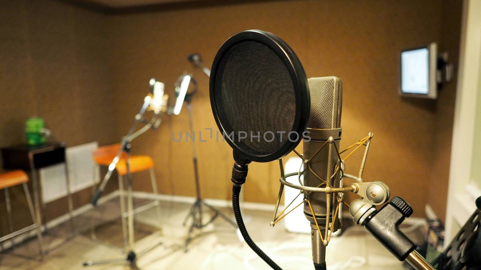 Microphone with shockmount and pop filter on tripod and note stand in recording sound studio video production.