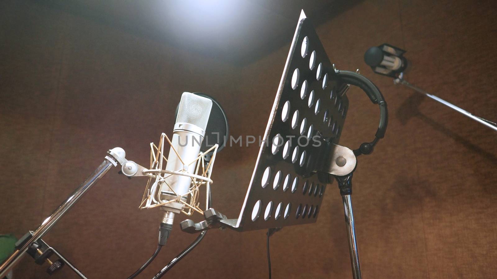 Microphone with shockmount and pop filter on tripod and note stand in recording sound studio video production.