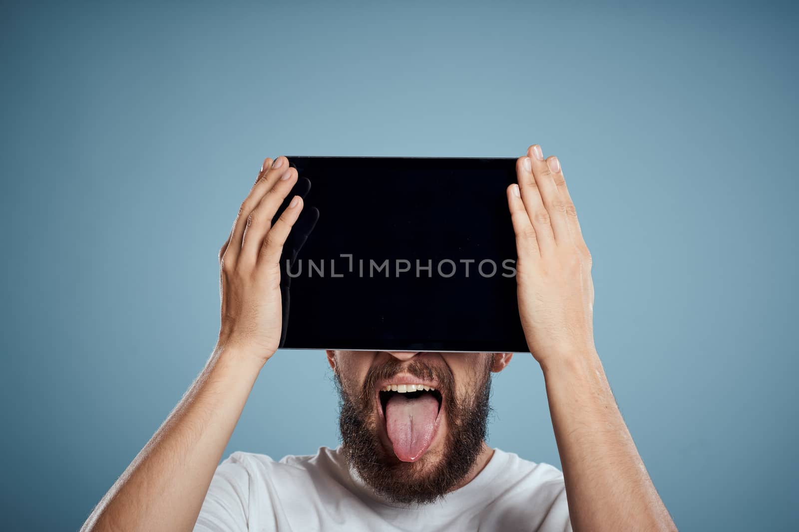man with touch tablet in front of face on blue background cropped view copy space emotions model. High quality photo