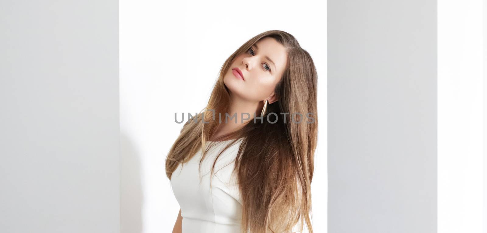 Young brunette with long wavy hairstyle in white interior, hair by Anneleven