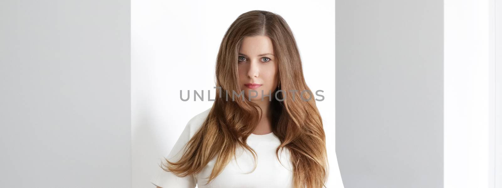 Young brunette with long wavy hairstyle in white interior, hair by Anneleven