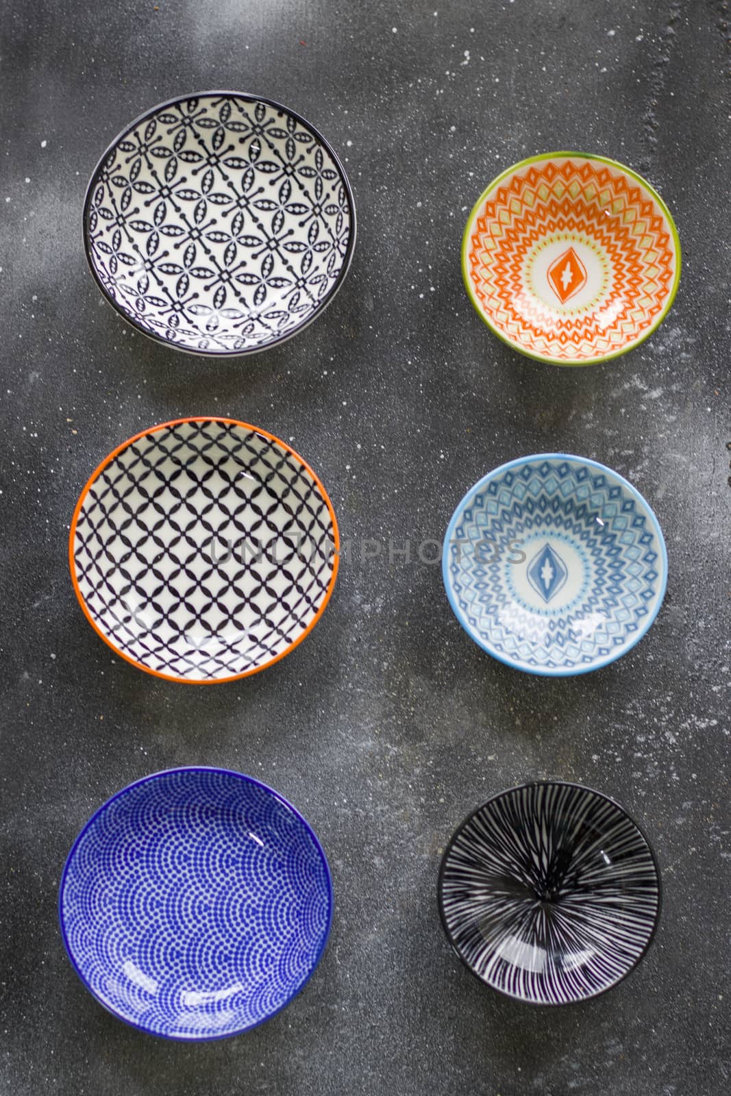 Colorful bowls on the black background, kitchen equipment on the table, bowl with geometric design.