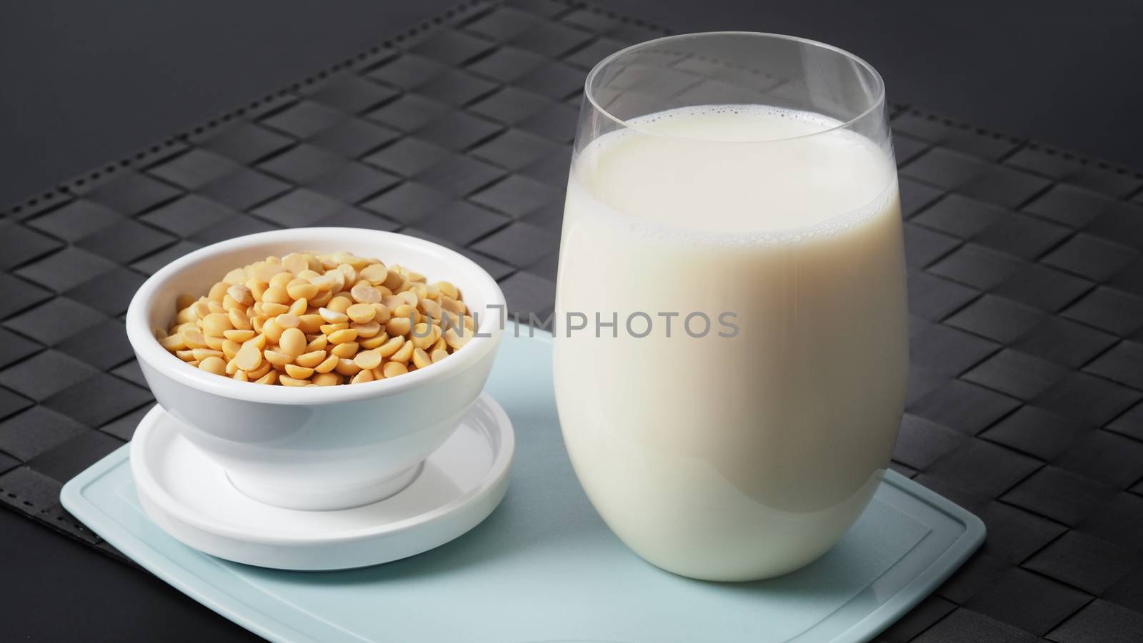 Close-up images of home made healthy drink soy milk with no sugar added in a glass on a green color plastic plate mat and soy beans in small bowl. All of them on black background in a studio shot.