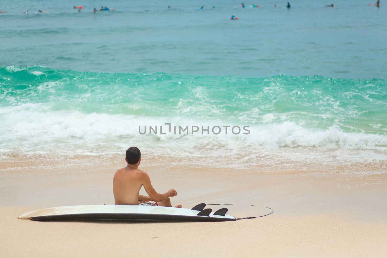 The guy is resting on a sandy tropical beach, after riding a surf. Healthy active lifestyle in summer vocation.