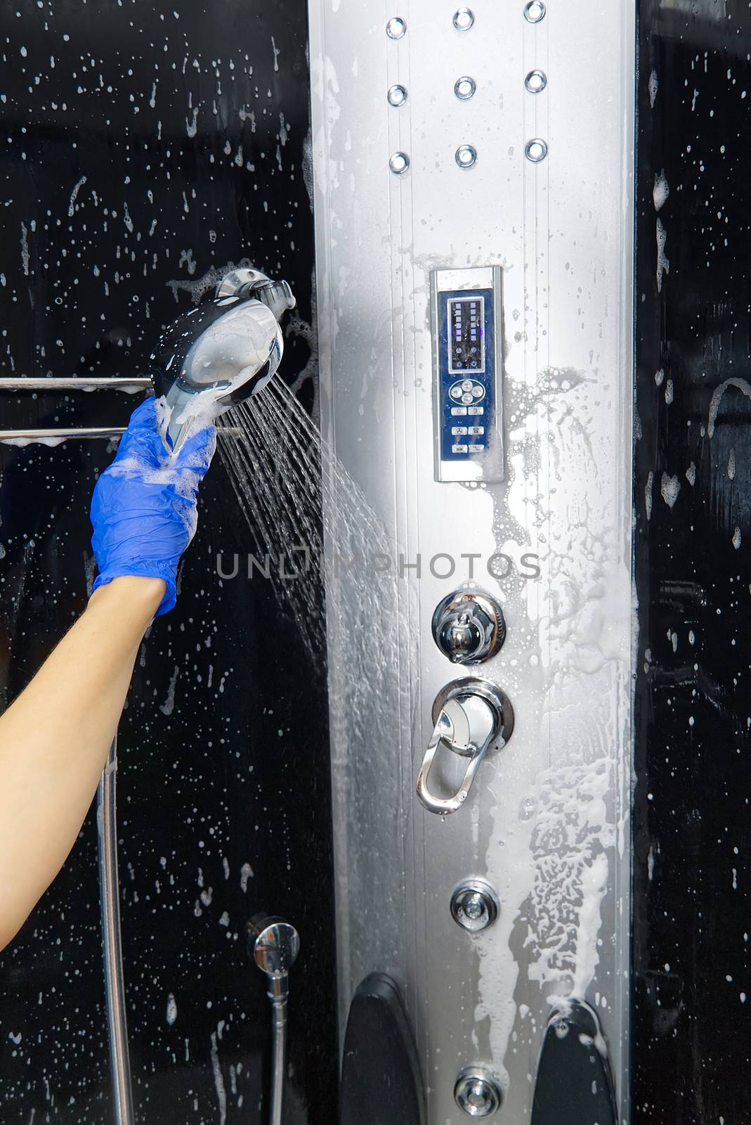 Cleaning of shower steam cabins from Calcium deposits. Cleaning in the bathroom. woman hand in blue gloves with rag and detergent, washing and polishing shower booth from Calcium stone. Maid or housewife cares about house. Commercial cleaning service company concept.