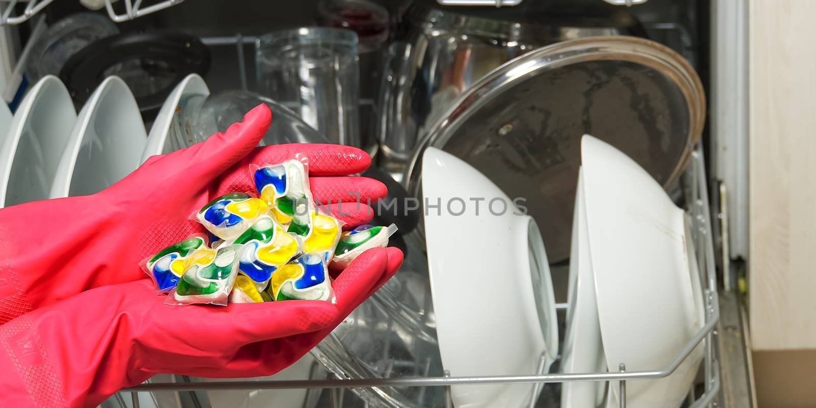 Dishwasher Detergents in hands. hands in pink golvs holds dishwasher gel capsules. Capsule for the dishwasher. Brilliant cleanliness. by PhotoTime