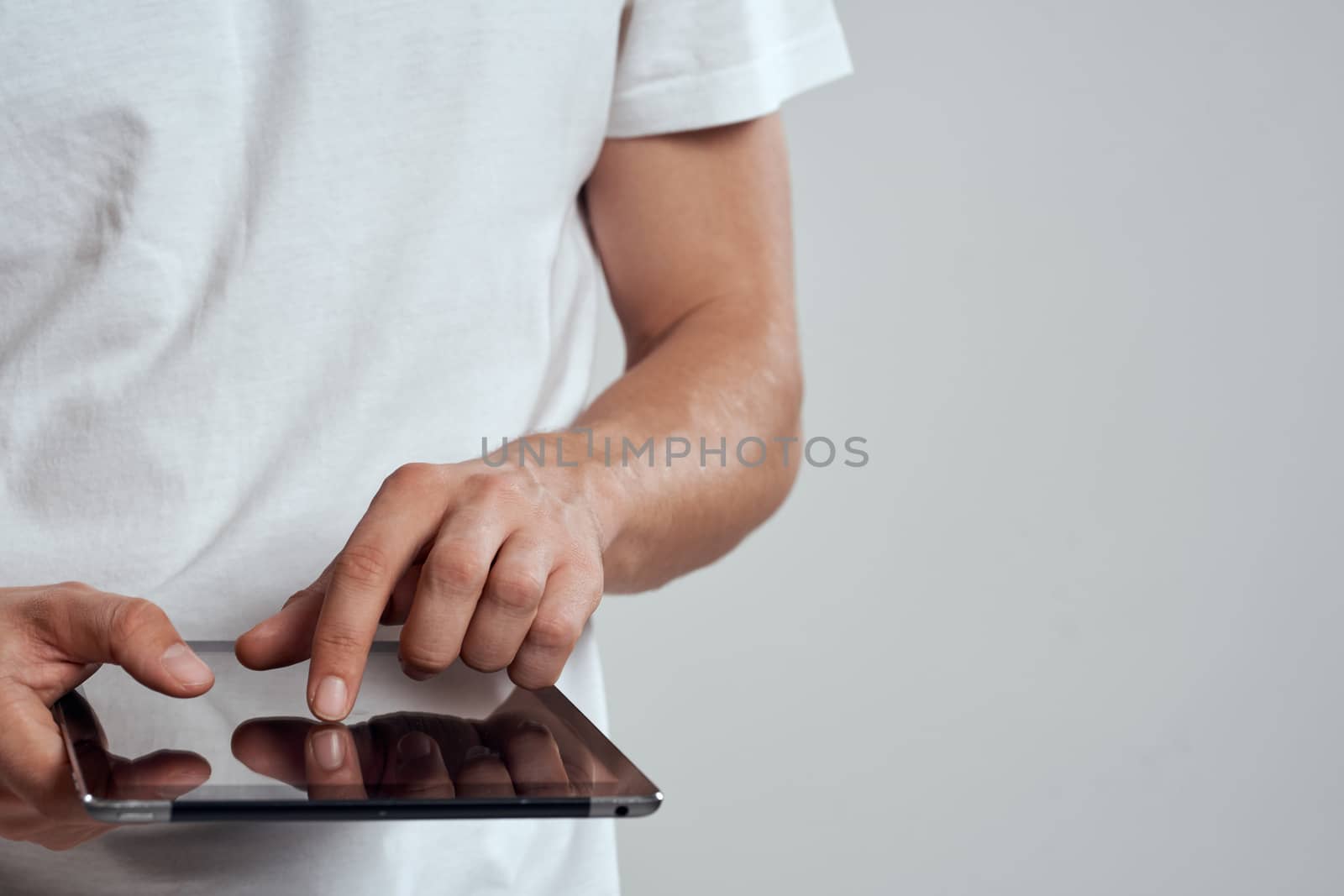 Tablet with a touch screen on a light background male hands white t-shirt cropped view by SHOTPRIME