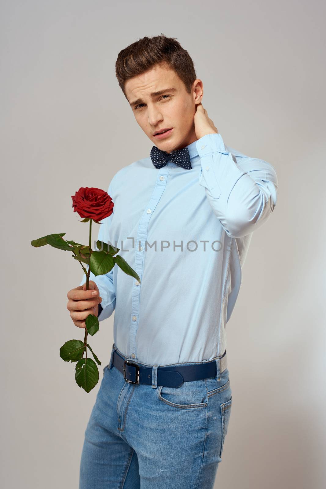 Romantic man with a red rose and in a blue shirt with a bow tie around his neck gray background by SHOTPRIME