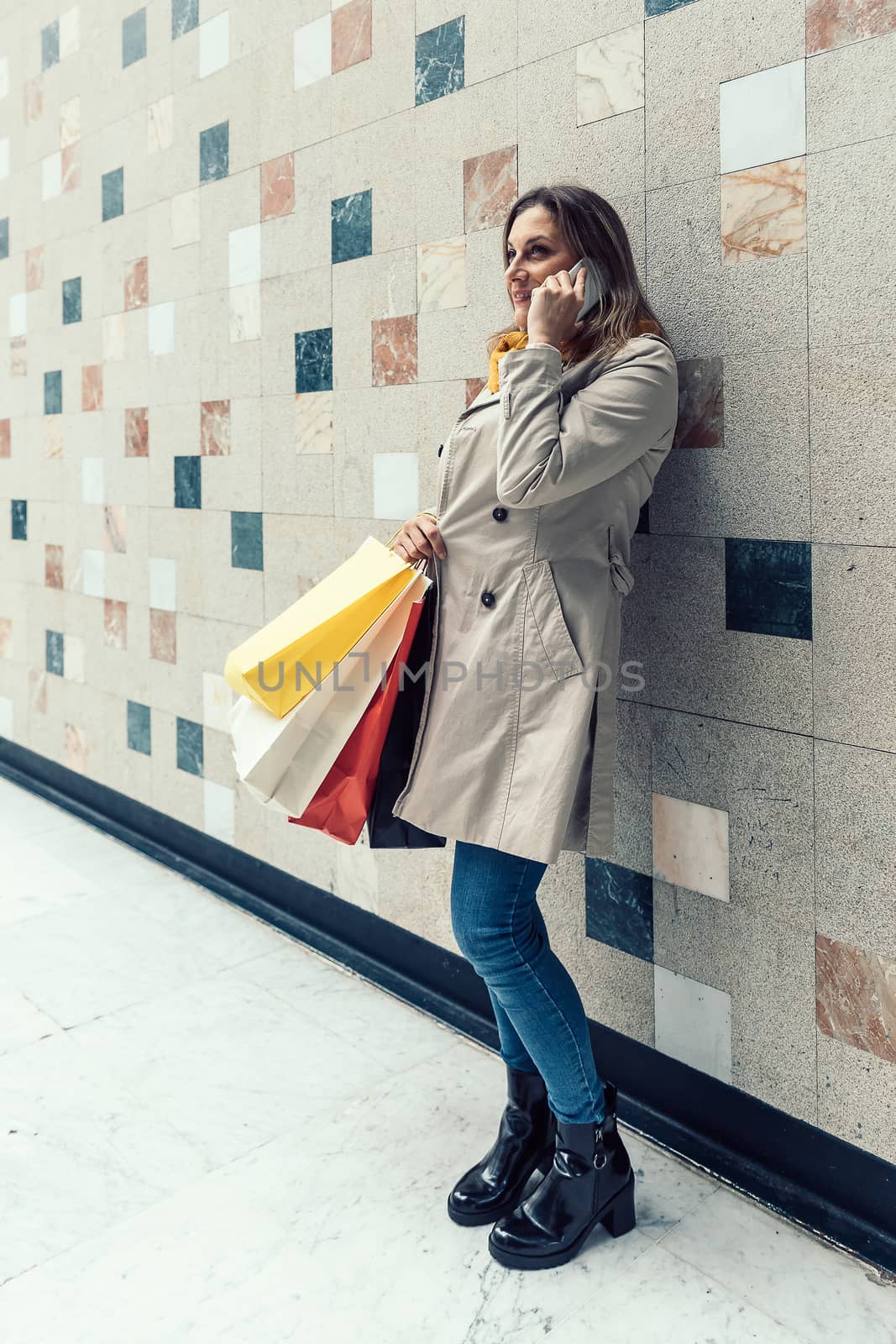 Adult woman talking on her mobile phone while holding shopping colorful bags. by JRPazos
