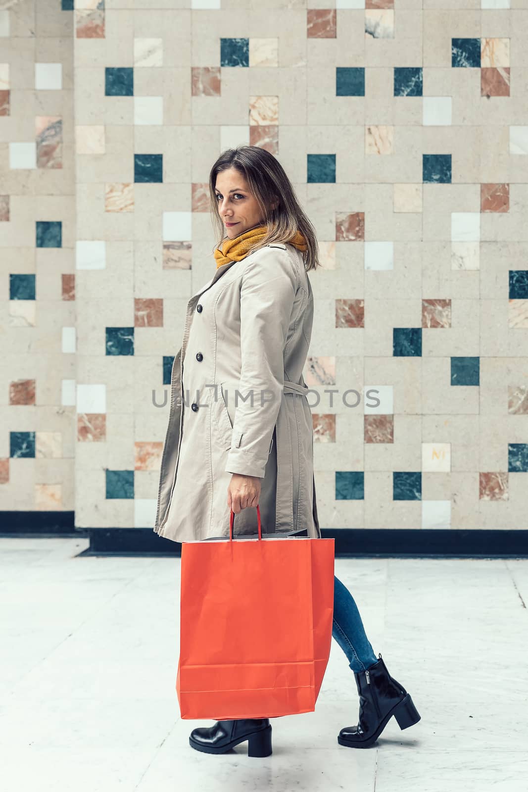 Adult caucasian woman walking alone through a mall with colorful shopping bags.