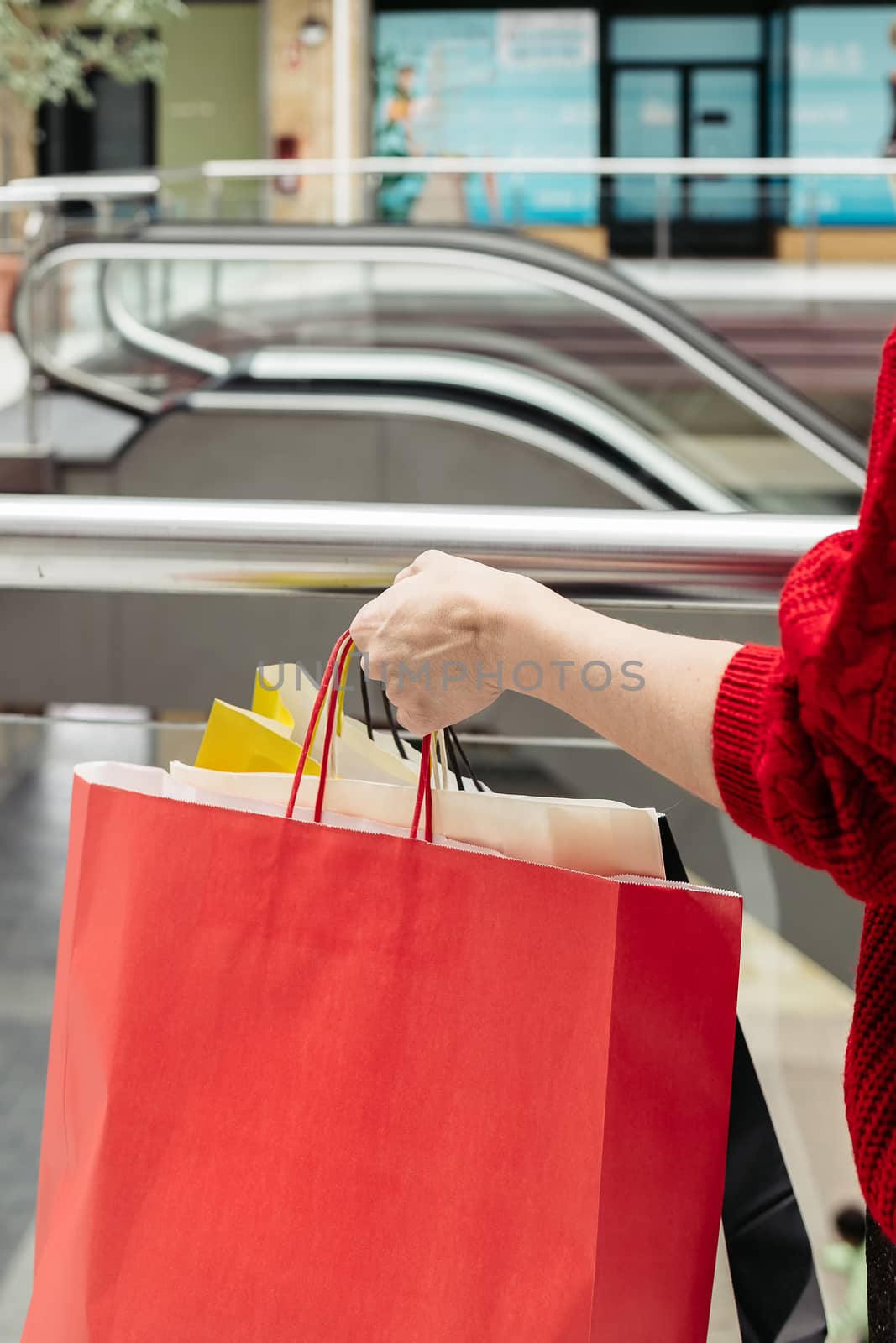 Close-up of a female hand holding colorful shopping bags in a mall.
