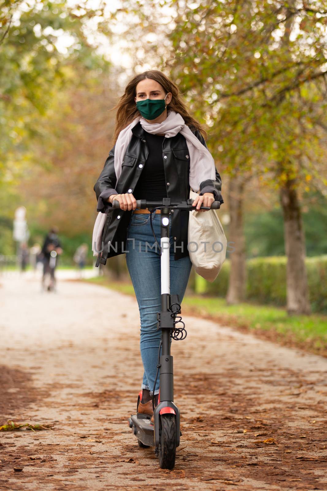Casual caucasian teenager wearing protective face mask riding urban electric scooter in city park during covid pandemic. Urban mobility concept by kasto