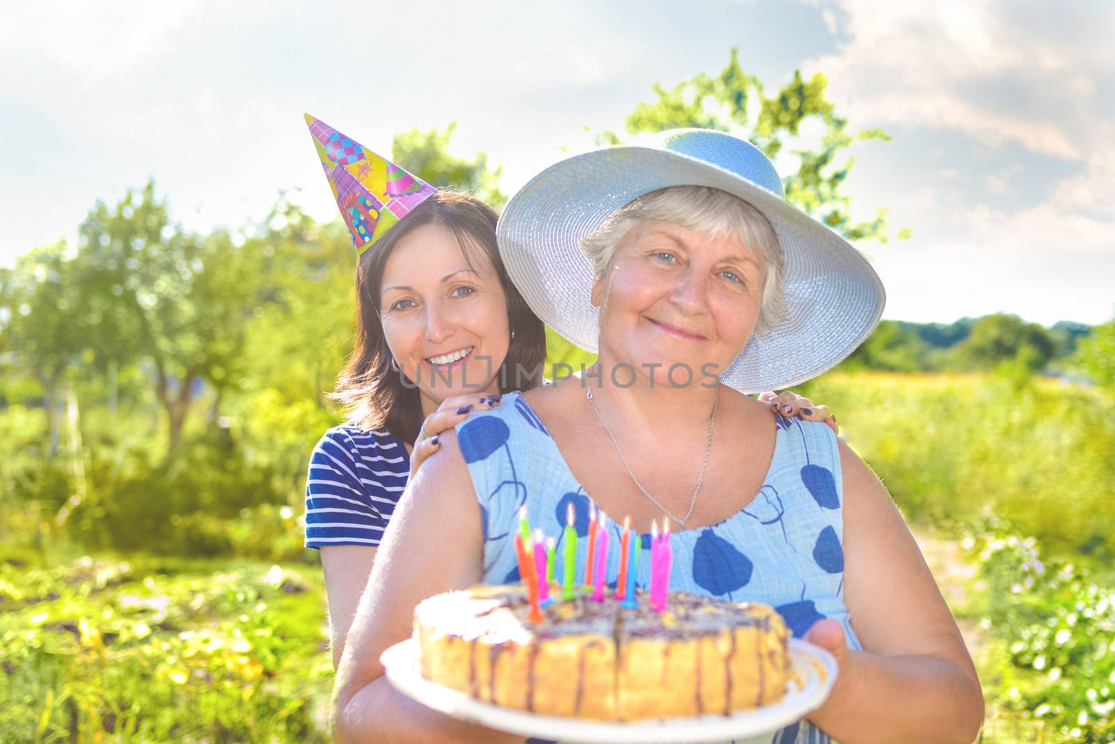 Grandmother's birthday, who with a smile, together with her daughter in the village and holds a birthday homemade cake.