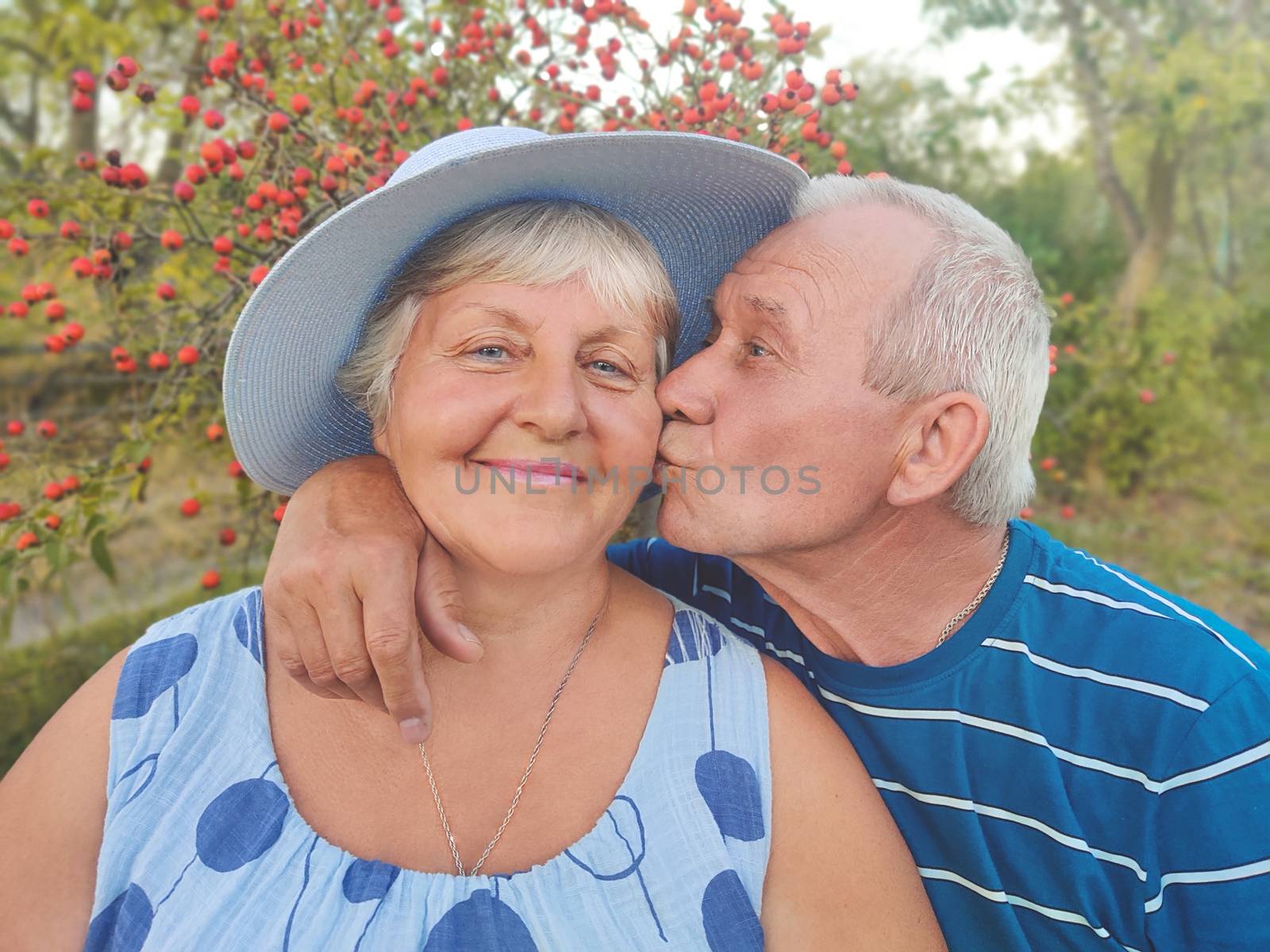 Authentic outdoor shot of aging couple having fun in the garden and blessed with love. During their game man is trying to kiss his partner and she is laughing out loud. Love and family concept. by Nickstock