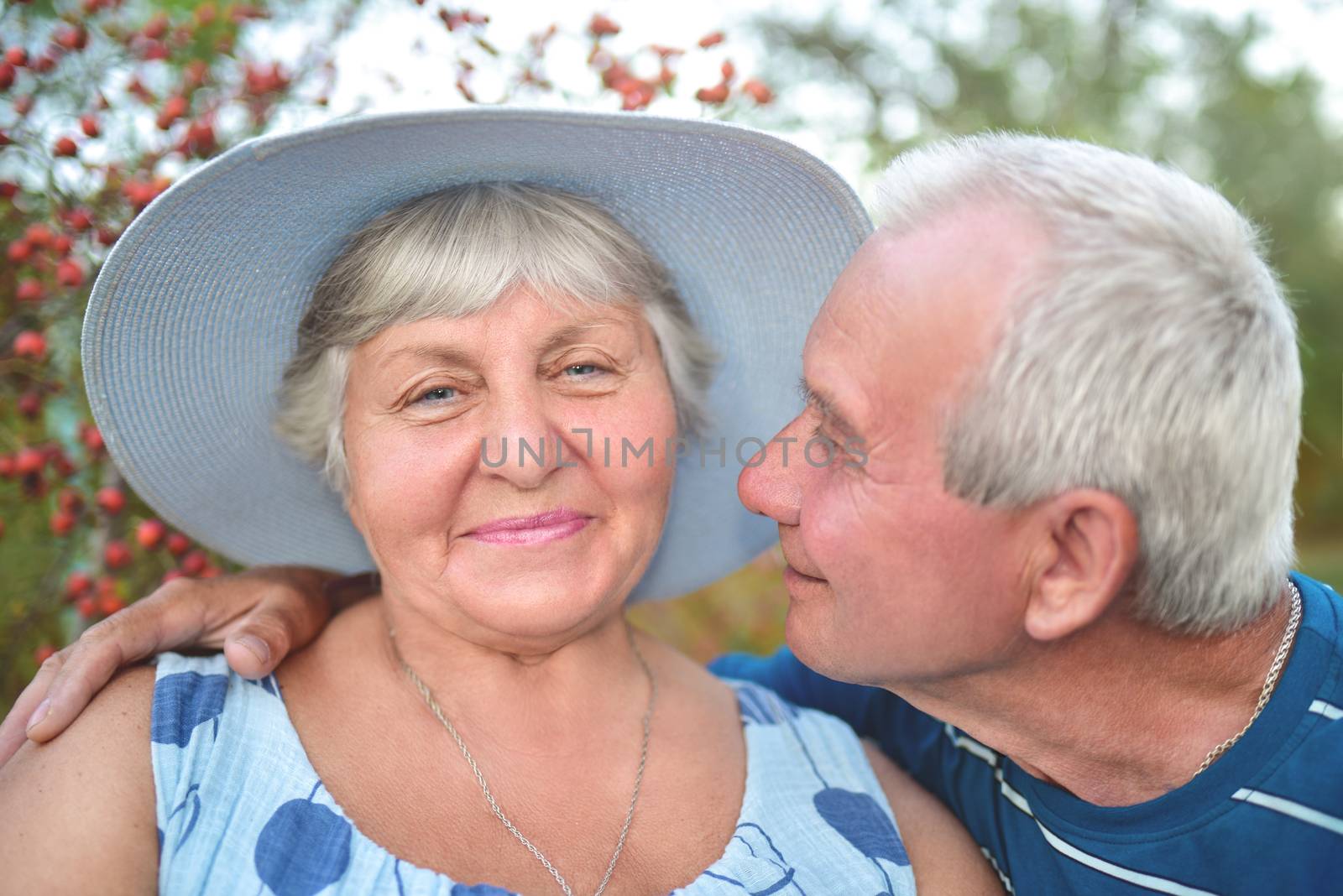 Authentic outdoor shot of aging couple having fun in the garden and blessed with love. During their game man is trying to kiss his wife and she is smiling. Love and family concept.