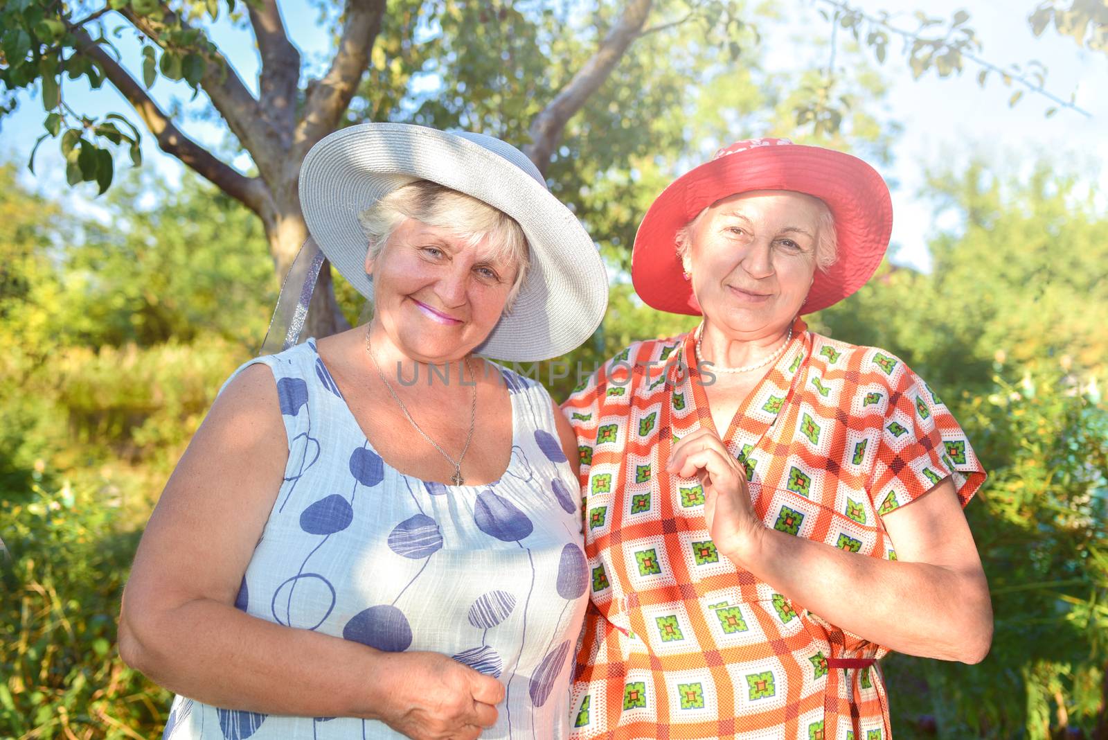 Walk in the garden. Two retired women best friends in hats walk happily in the garden. by Nickstock