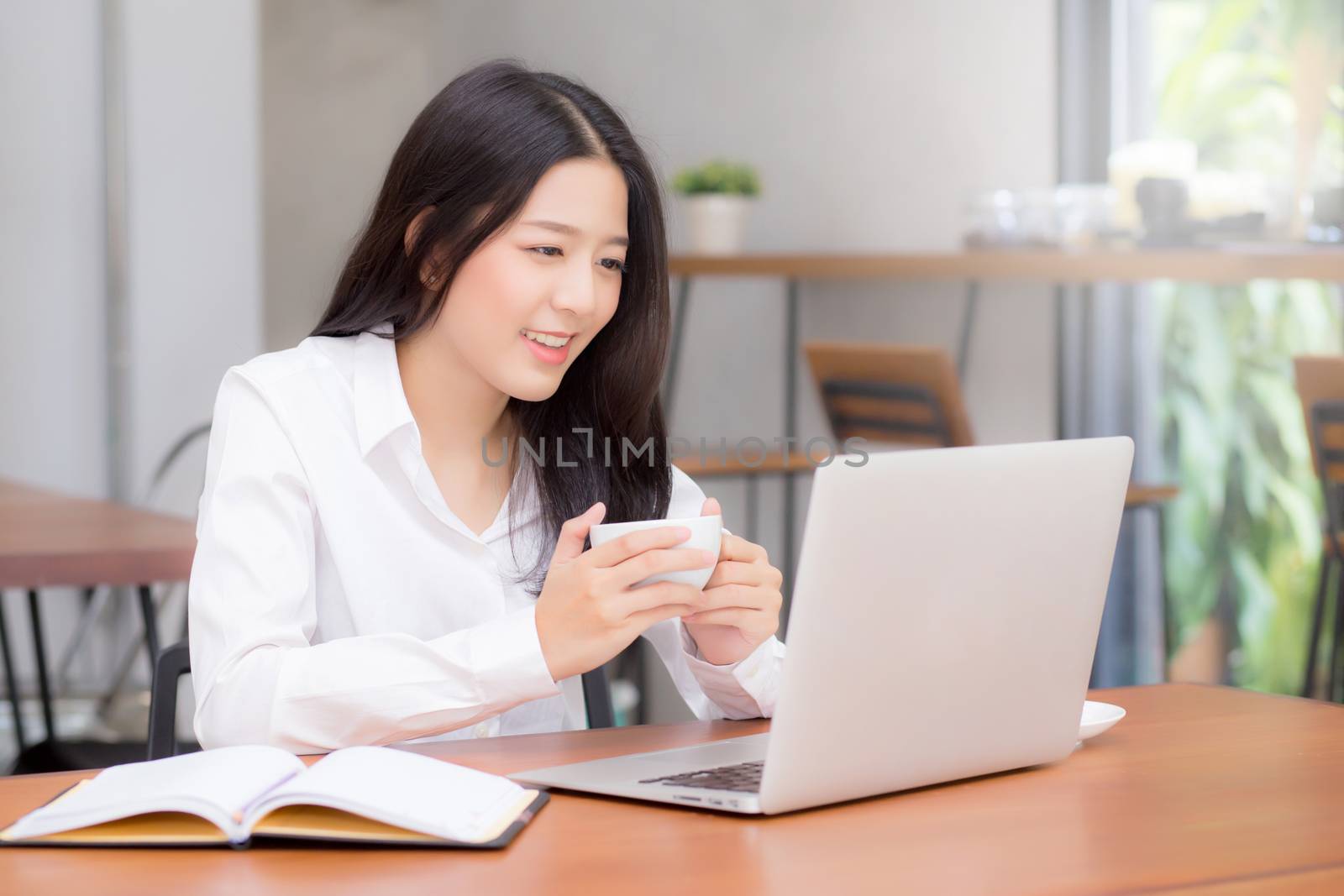 Beautiful asian young woman working online on laptop sitting at coffee shop, professional female freelancer using notebook computer with connect to internet for distance job.