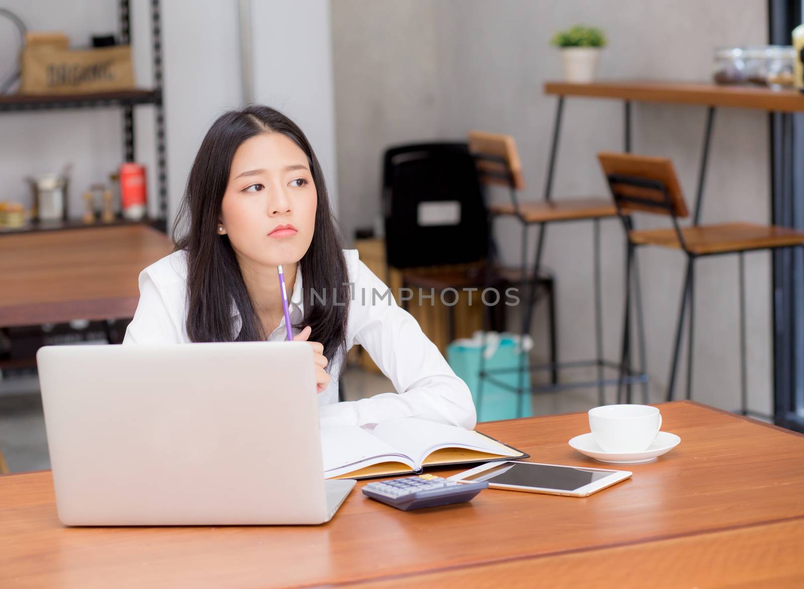 Asian young woman working online with laptop and think project for idea at modern cafe shop, business and freelance concept.