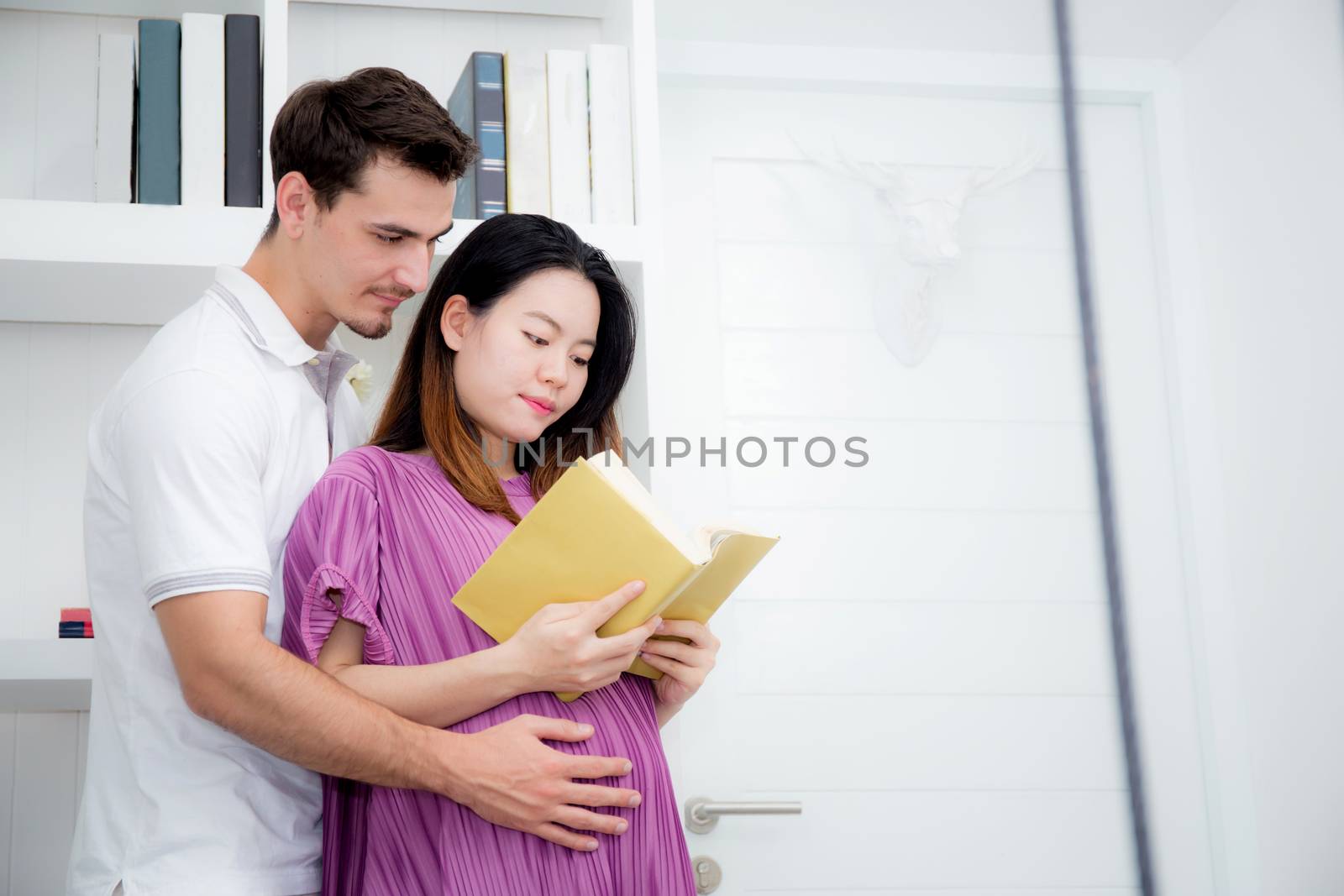 Husband with pregnant woman reading yellow book together, Portrait of couple with hug, happy with family choose name newborn concept.
