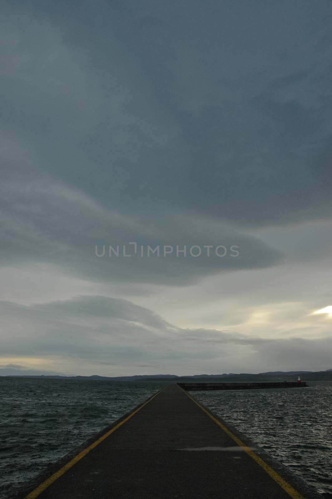 Long jetty path leads to the grey stormy ocean in evening by eyeofpaul