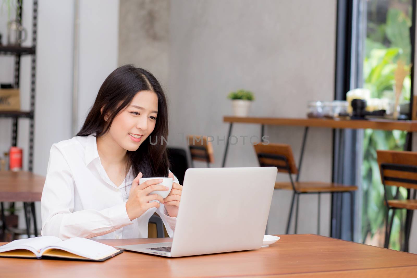 Beautiful asian young woman working online on laptop sitting at coffee shop, professional female freelancer using notebook computer with connect to internet for distance job.