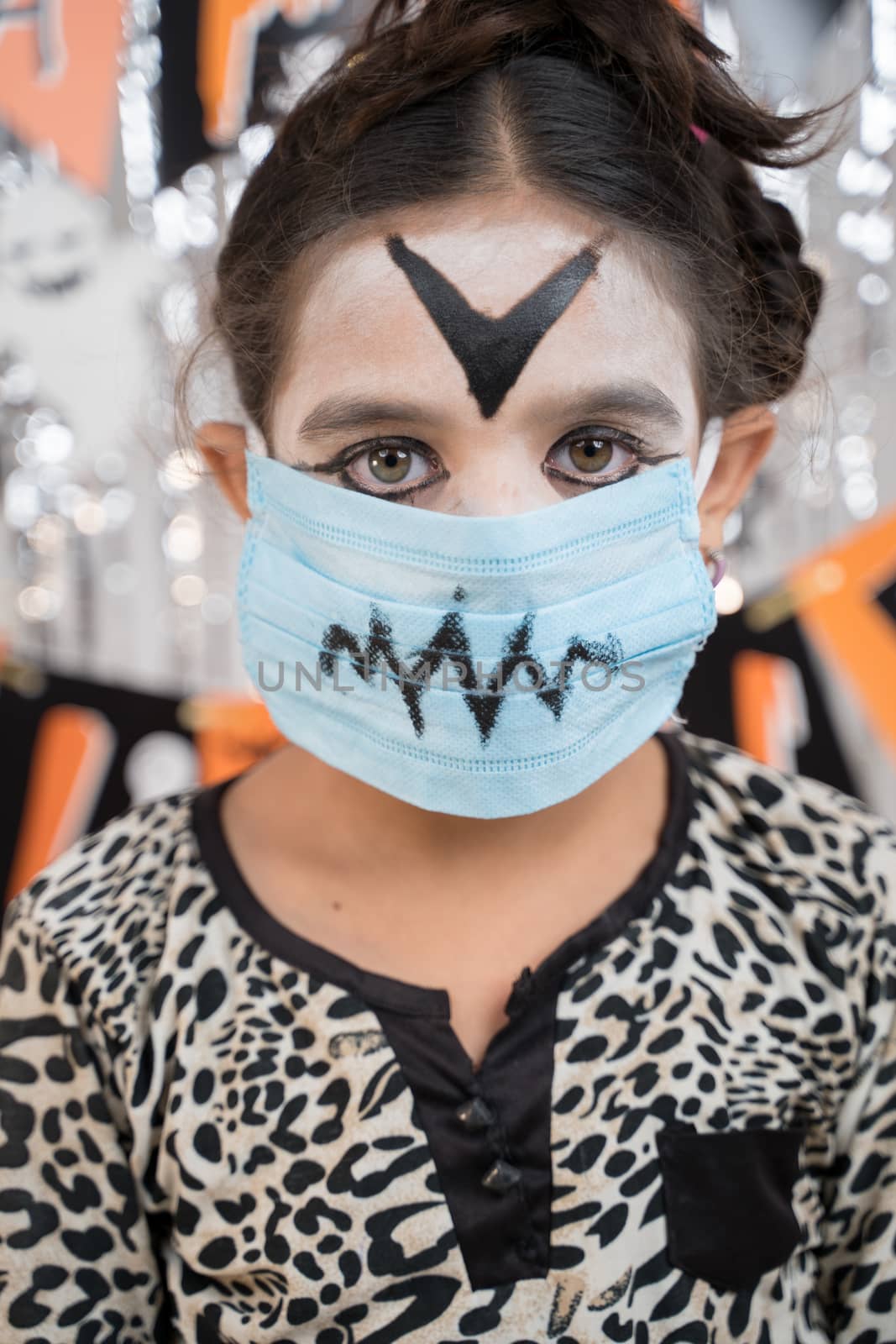 Kid in Halloween witch dress and scary face with medical mask looking into camera - halloween celebration during pandemic. by lakshmiprasad.maski@gmai.com