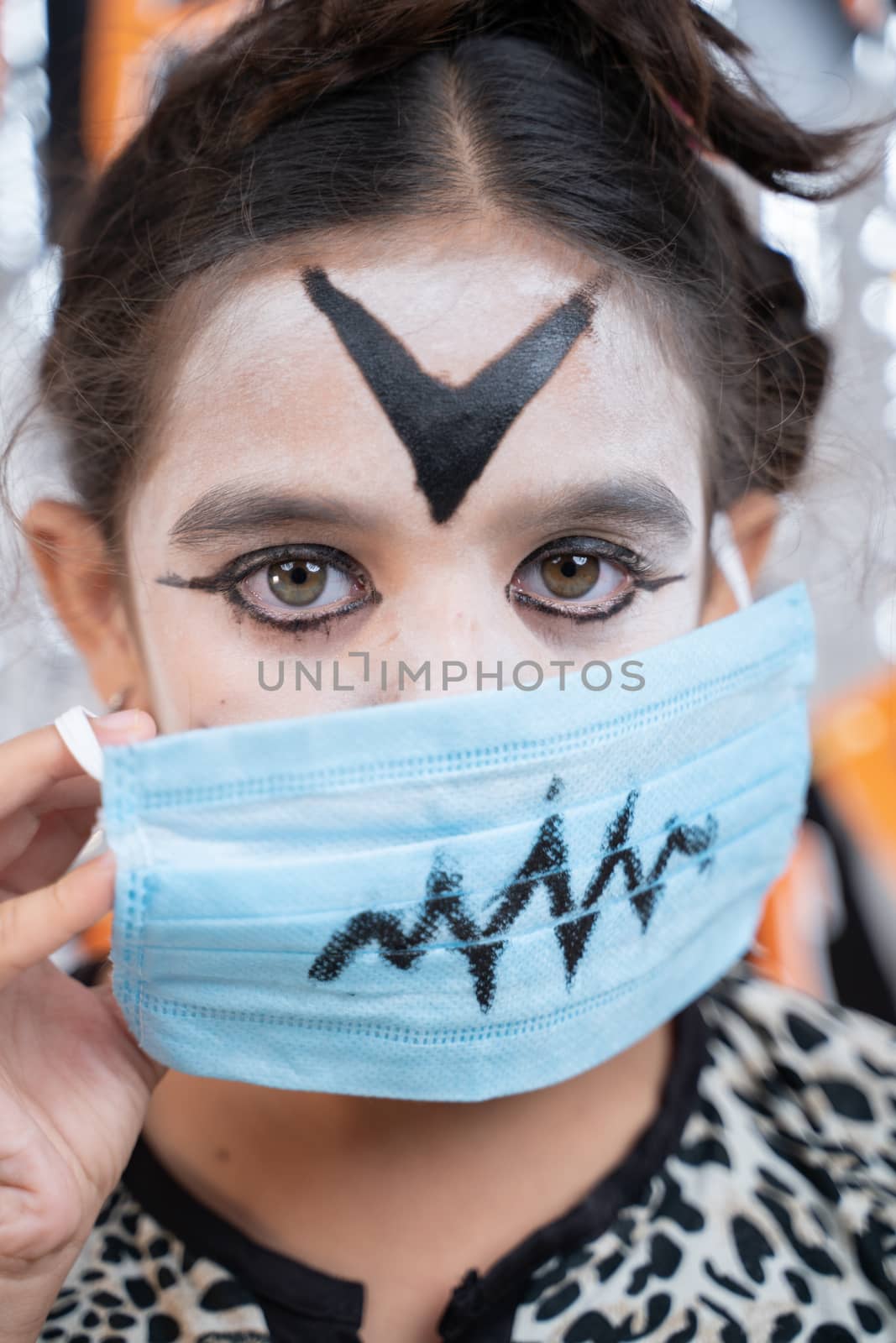 Close up Vertical shot of Kid in Halloween witch dress and scary face removing medical mask by looking into camera by lakshmiprasad.maski@gmai.com