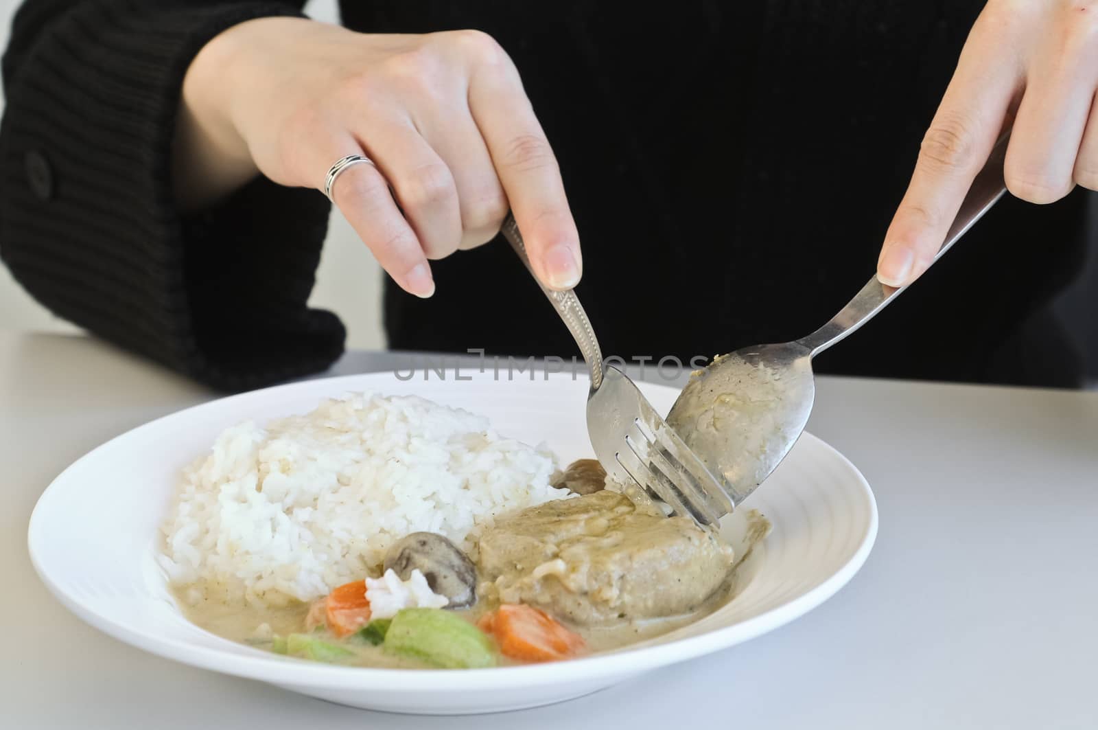 A lady eating curry rice with spoon and fork