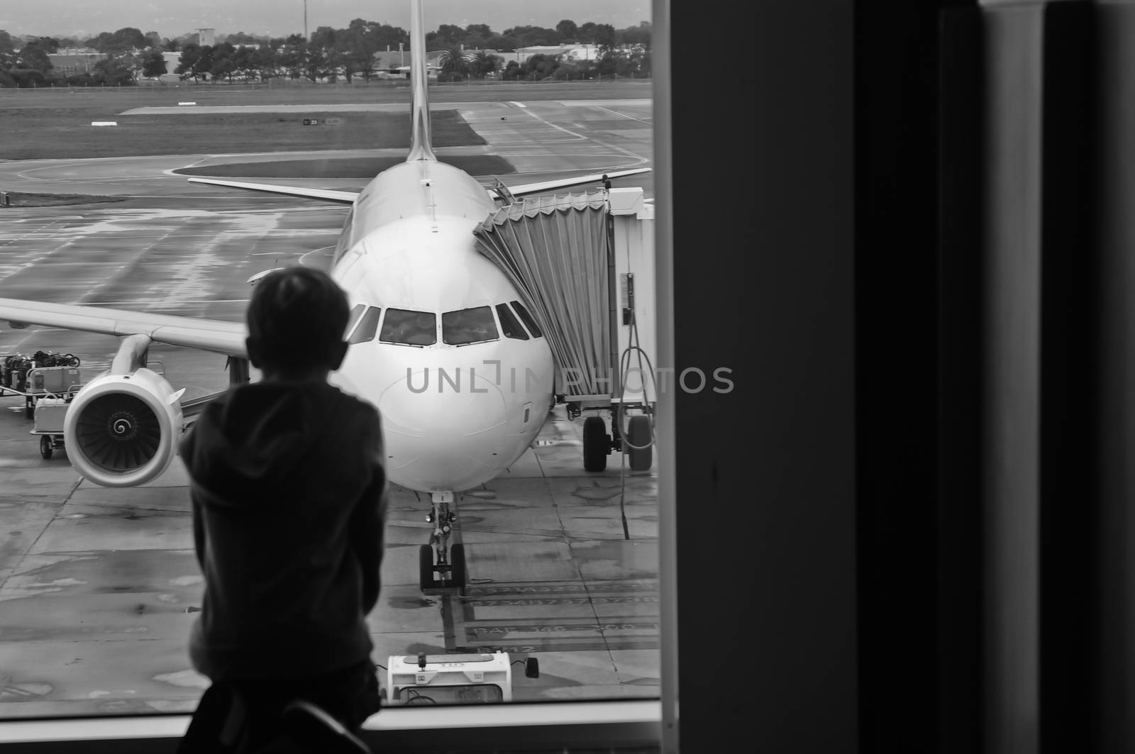 A child is sitting and looking for a plane at the airport in monochrome tone