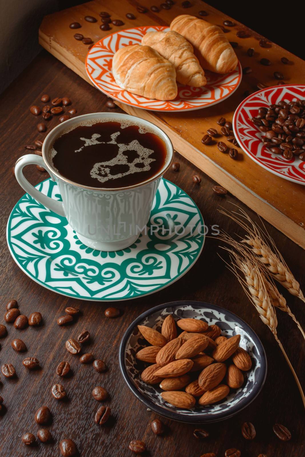 breakfast with breads and coffee on wooden table with coffee beans and almonds under daylight in 45 degrees