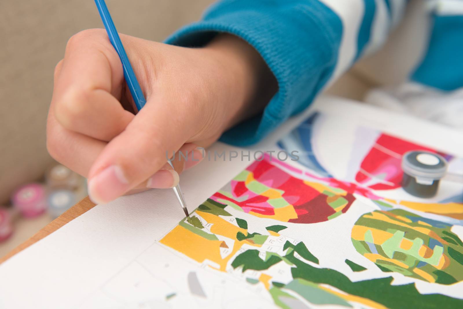 6 - Multicolored close up of painting by numbers. Young and bright female hand holds the bright blue paintbrush with detail as it paints green