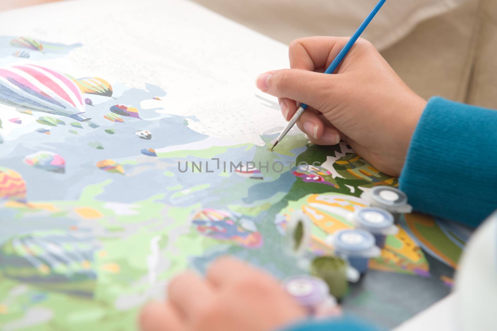 11 - Hot air balloon painting by numbers artwork. Being painted by young person with tanned skin. Blue jumper and paintbrush colors pop against skin